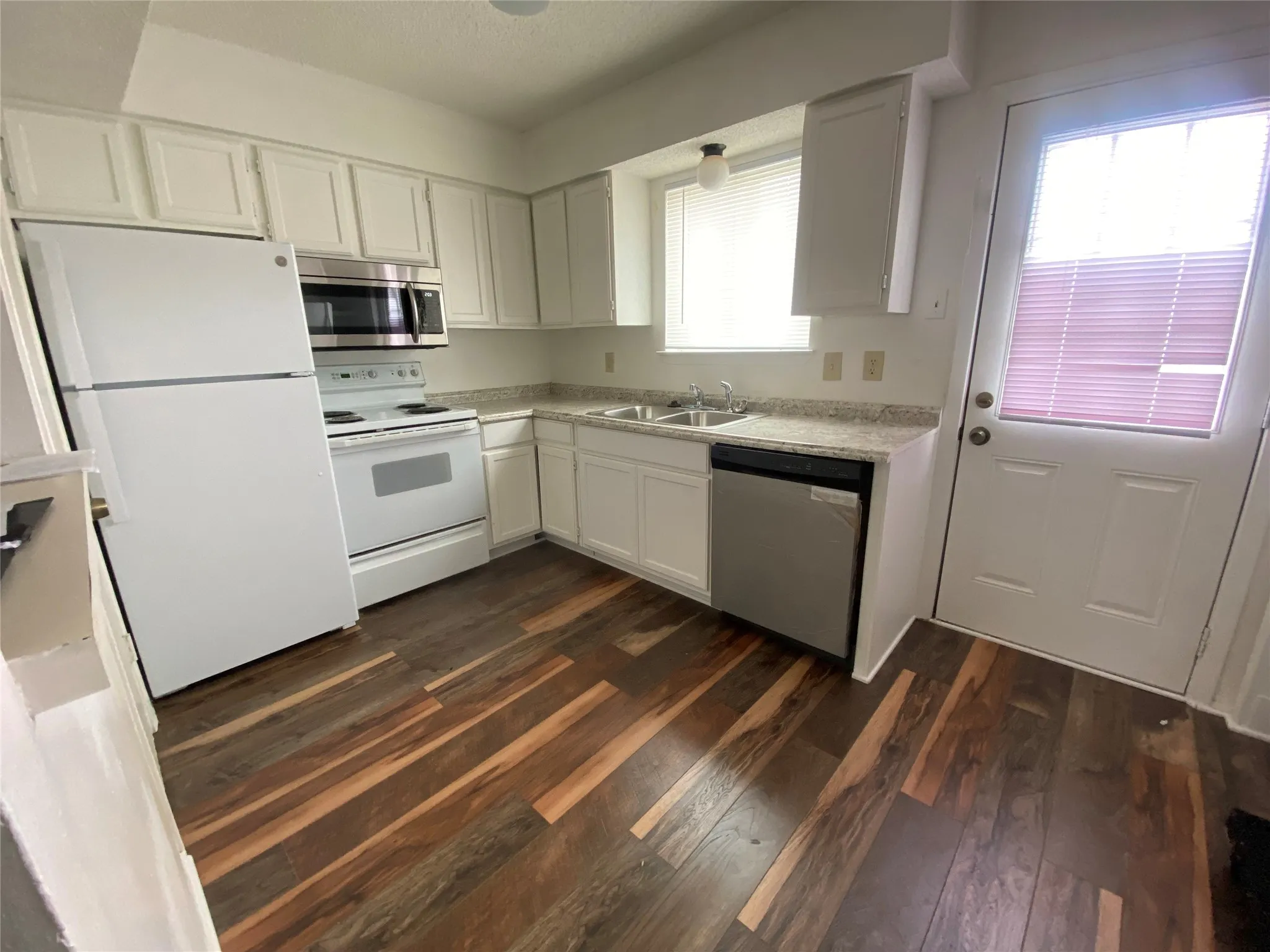 Kitchen featuring stainless steel appliances, light countertops, white cabinets, a sink, and dark wood-type flooring