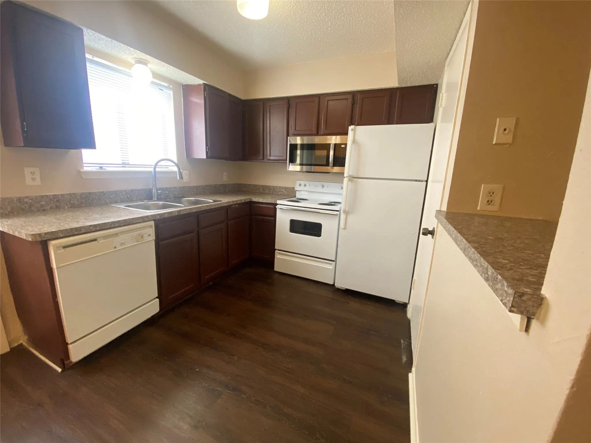 Kitchen with a textured ceiling, white appliances, dark wood-style floors, and a sink