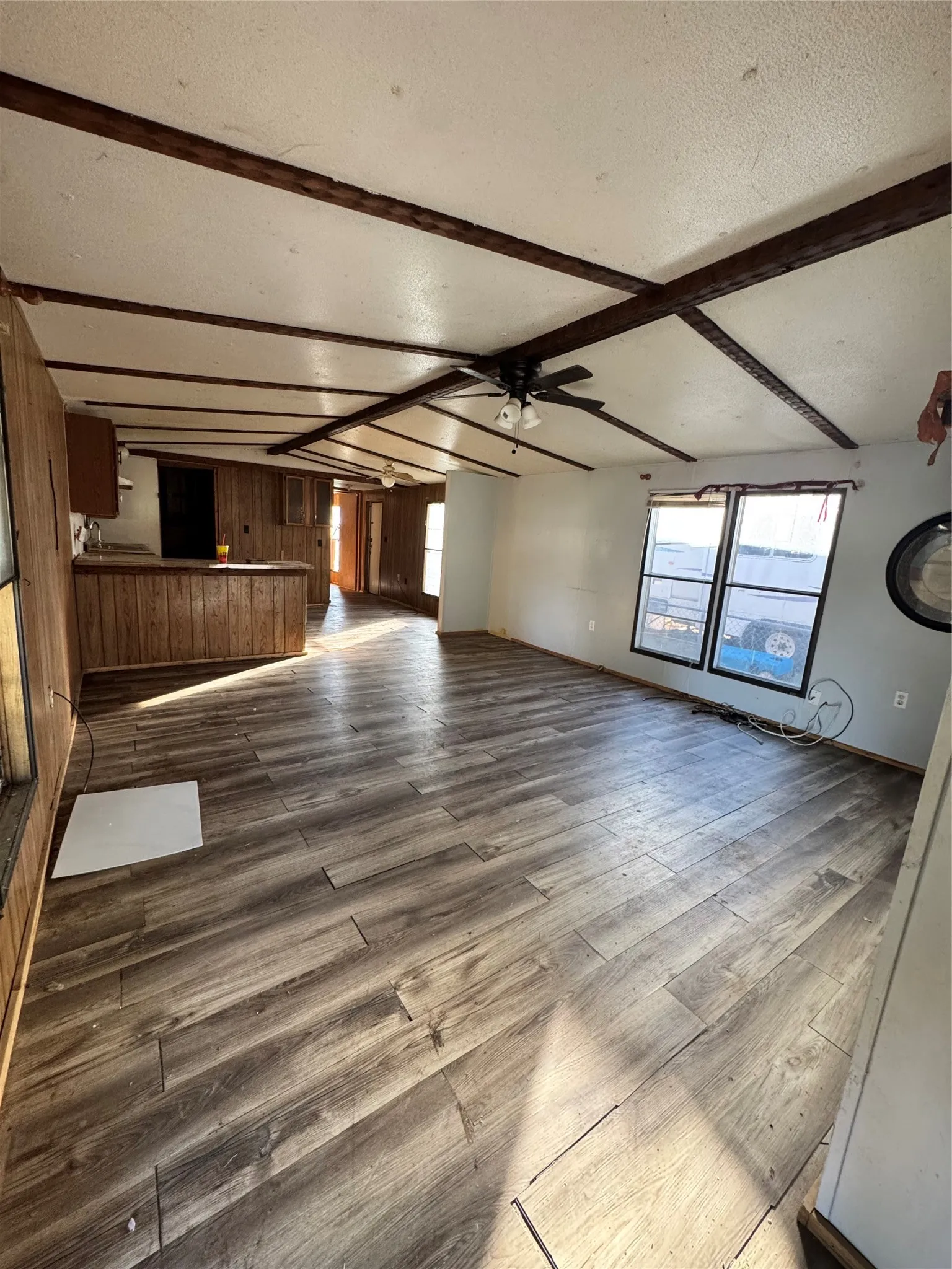 Spacious room featuring wood-finish flooring, exposed ceiling beams, and a ceiling fan with integrated lighting