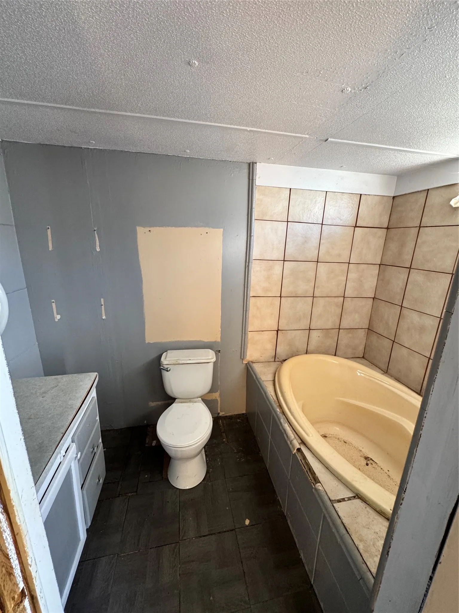 Built-in bathtub with tiled surround, white toilet, vanity with integrated sink, and dark-toned floor tiles