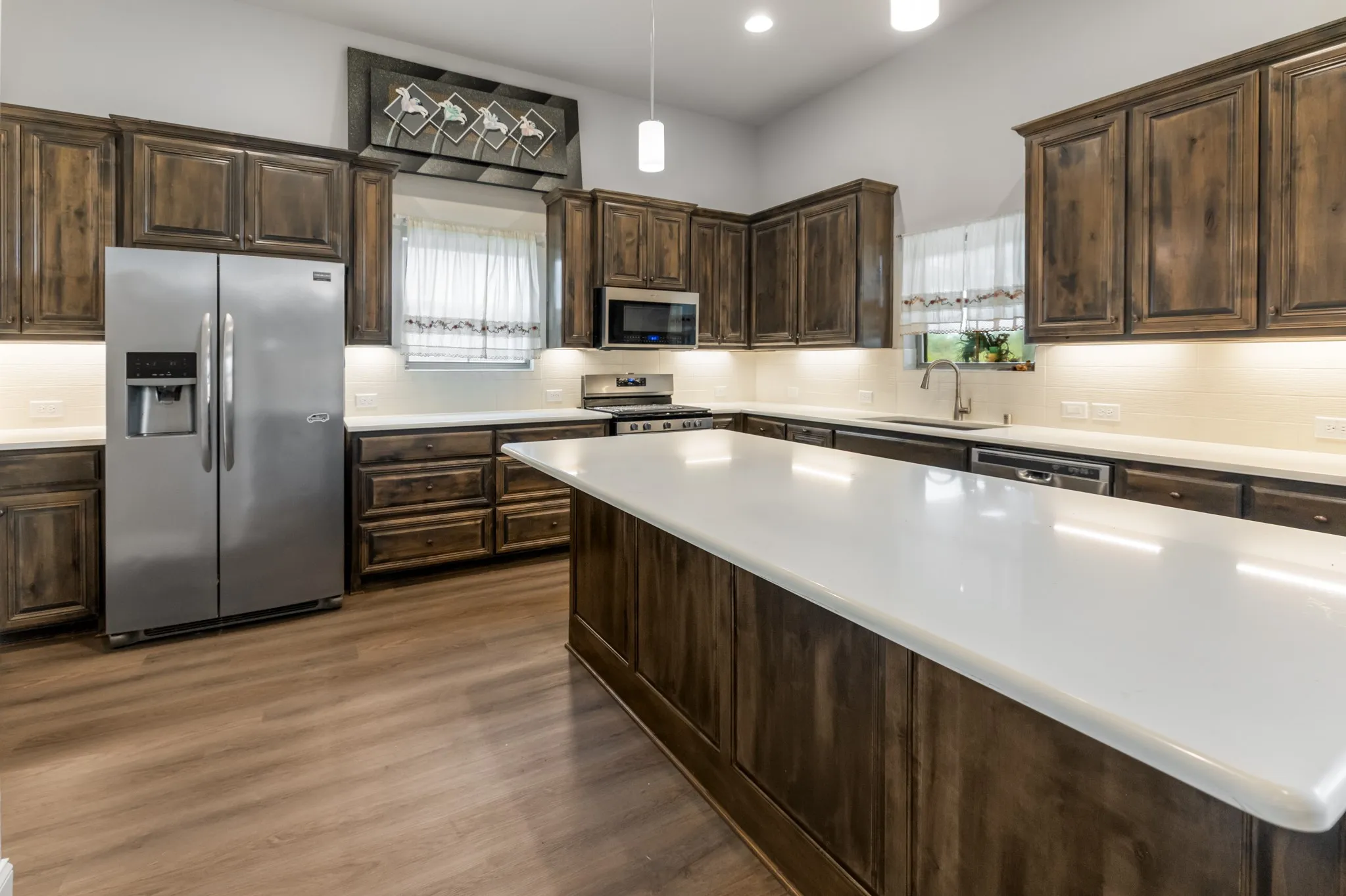 Spacious kitchen featuring wood-finish cabinetry, stainless steel appliances, a large center island with a white countertop, and wood-finish flooring