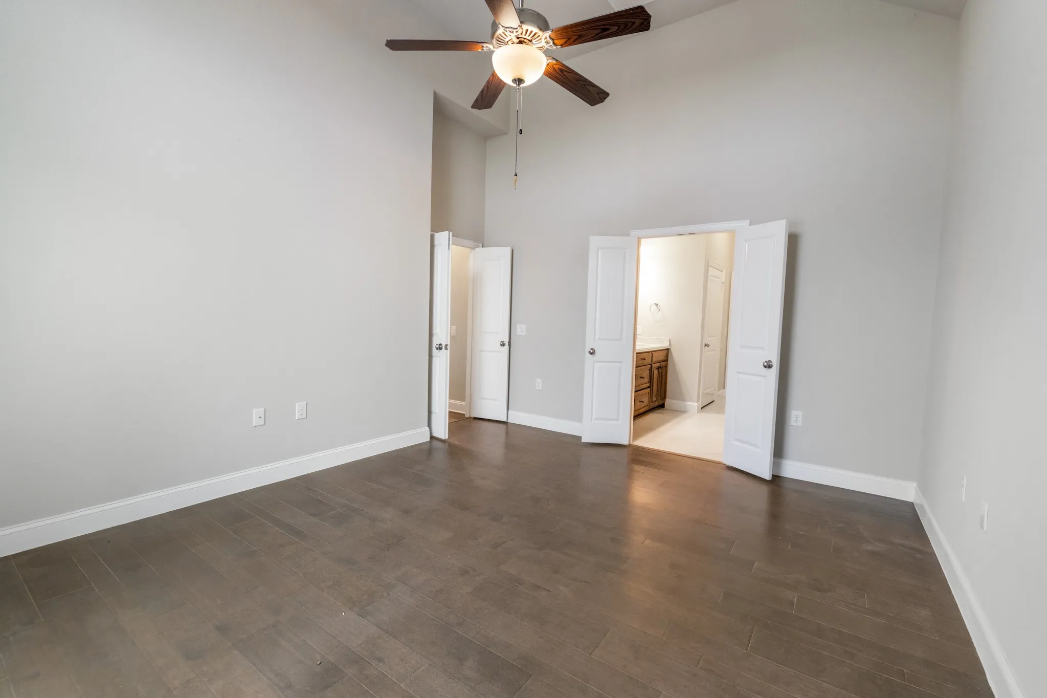 Vaulted ceiling with a ceiling fan, wood-finish flooring, light gray wall paint, and white trim