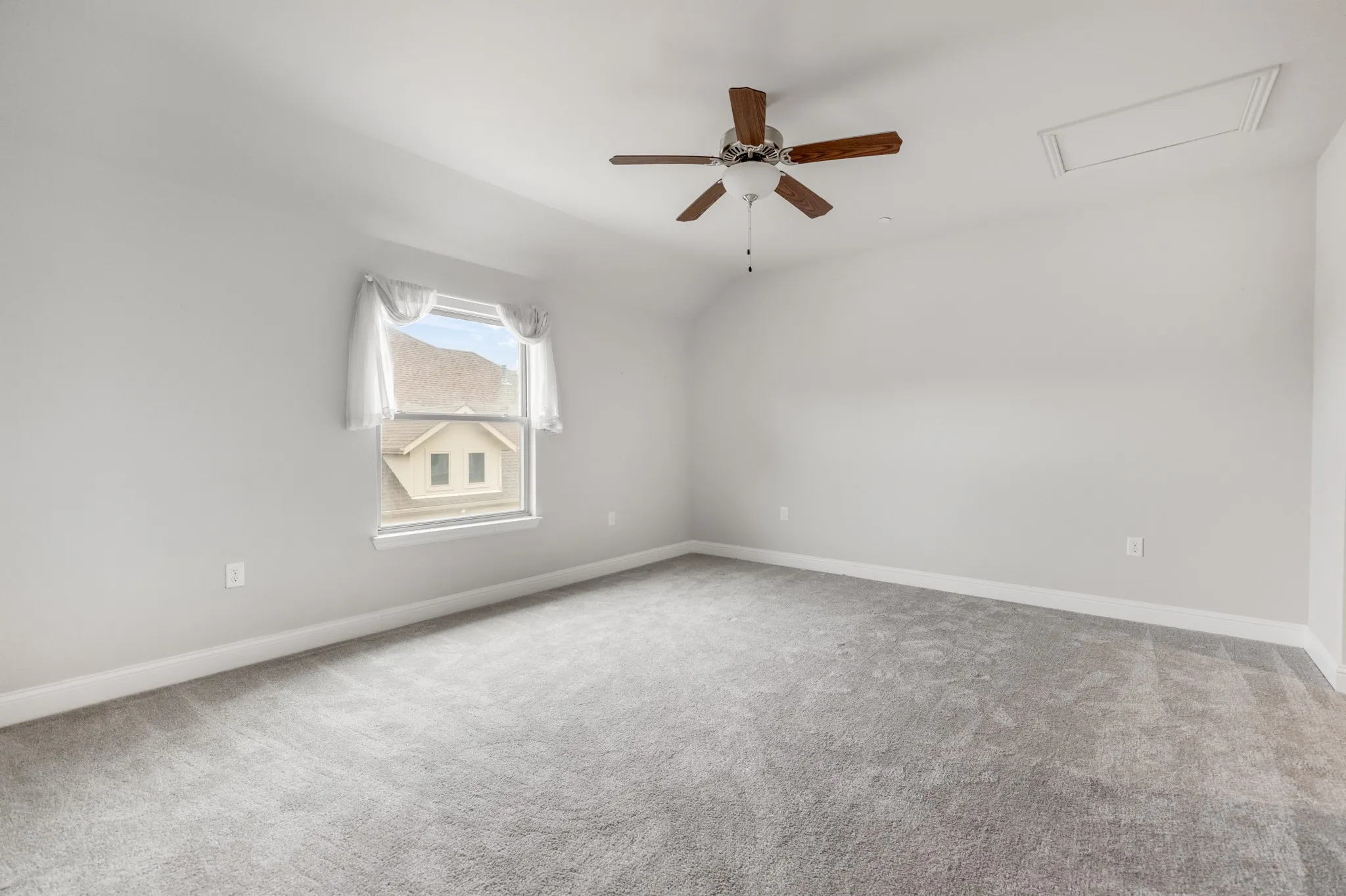 Spacious room with gray carpeting, white walls, a ceiling fan, and a window