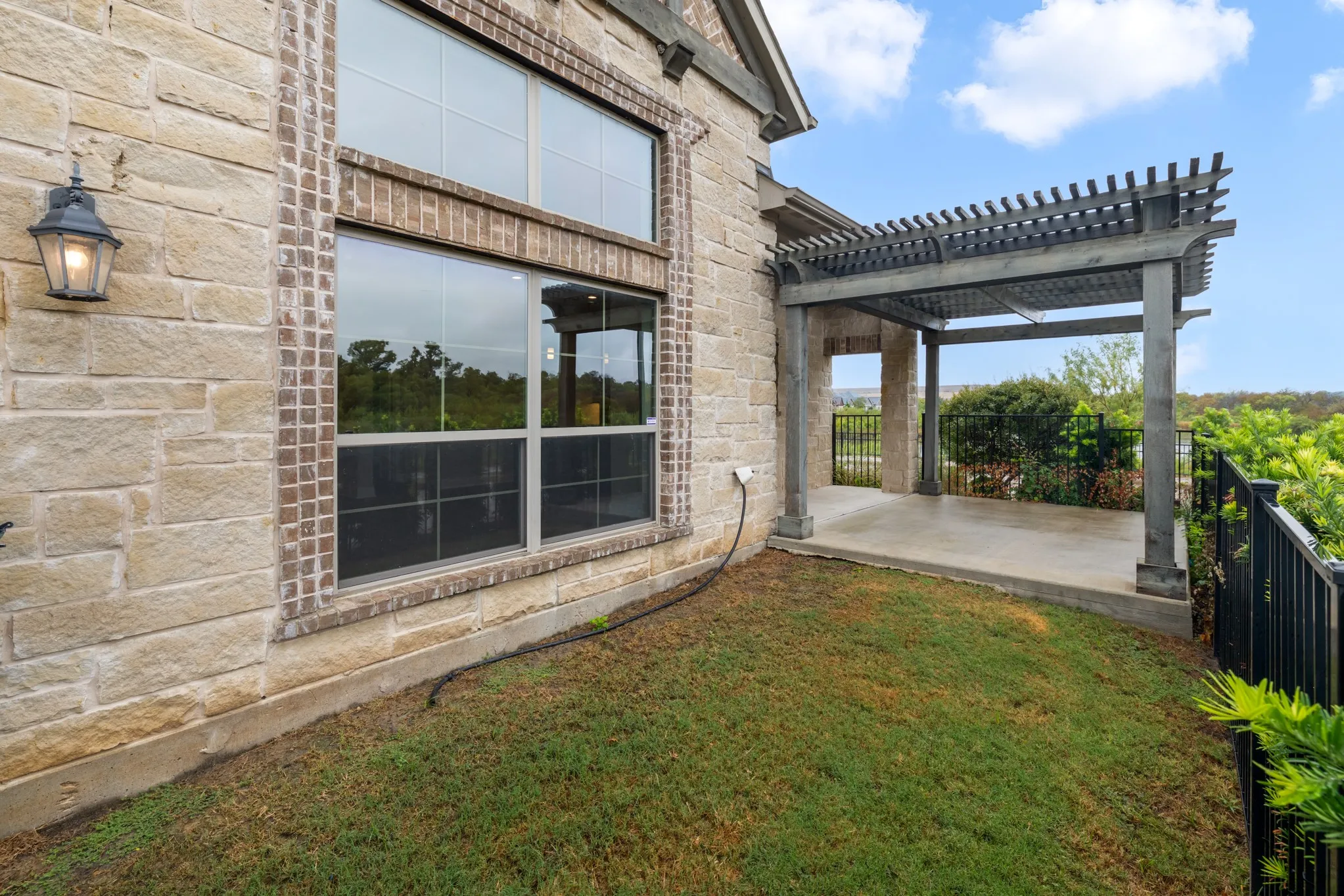Stone and brick exterior with a pergola-covered patio, surrounded by a black metal fence