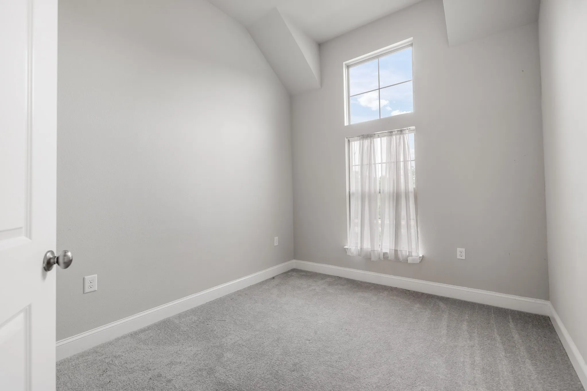 Vaulted ceiling with architectural detail, light gray wall paint, gray carpet flooring, and a multi-pane window configuration