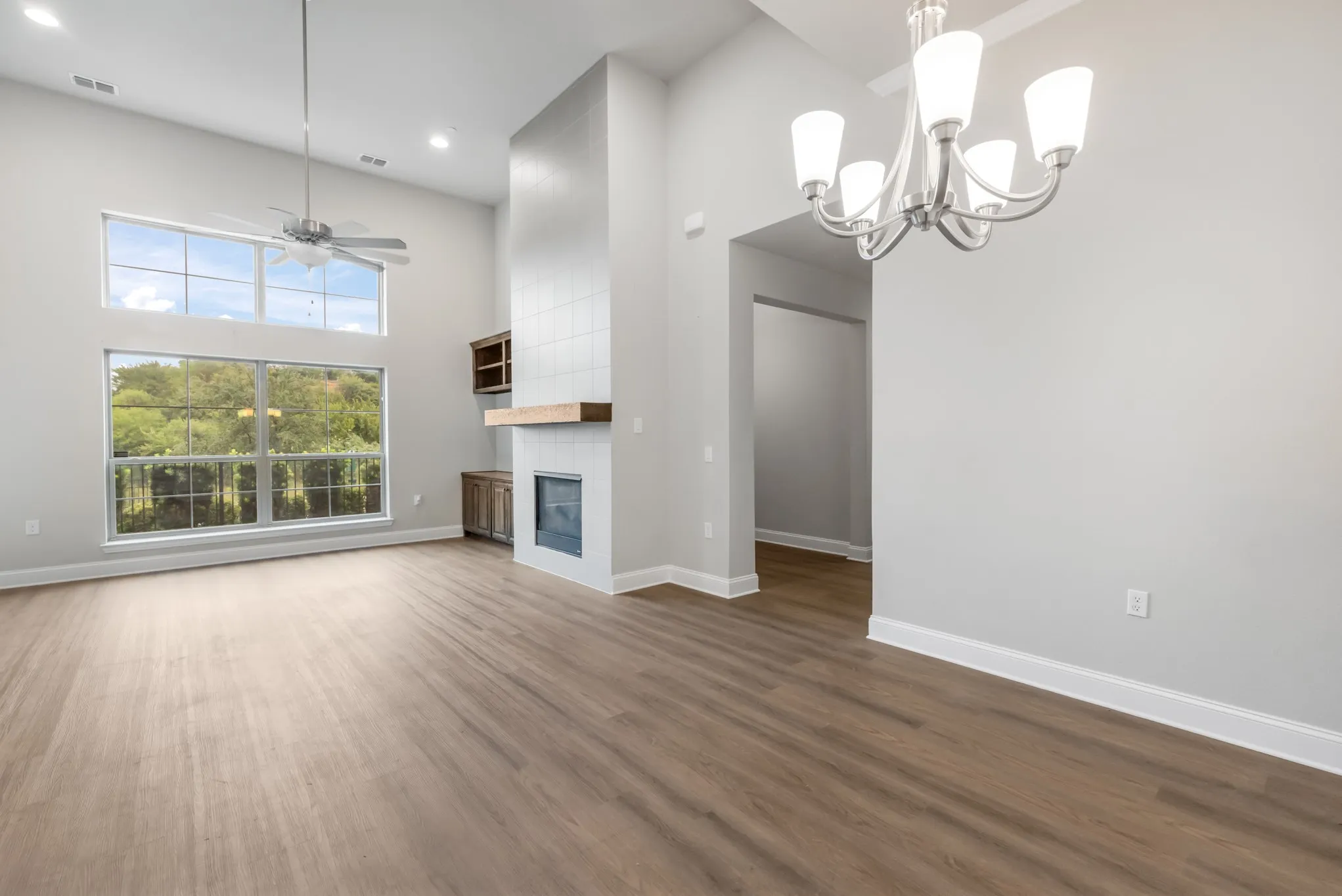 Two-story vaulted ceiling with a contemporary ceiling fan, large windows, wood-finish flooring, tiled fireplace with a wood mantle, and built-in cabinetry
