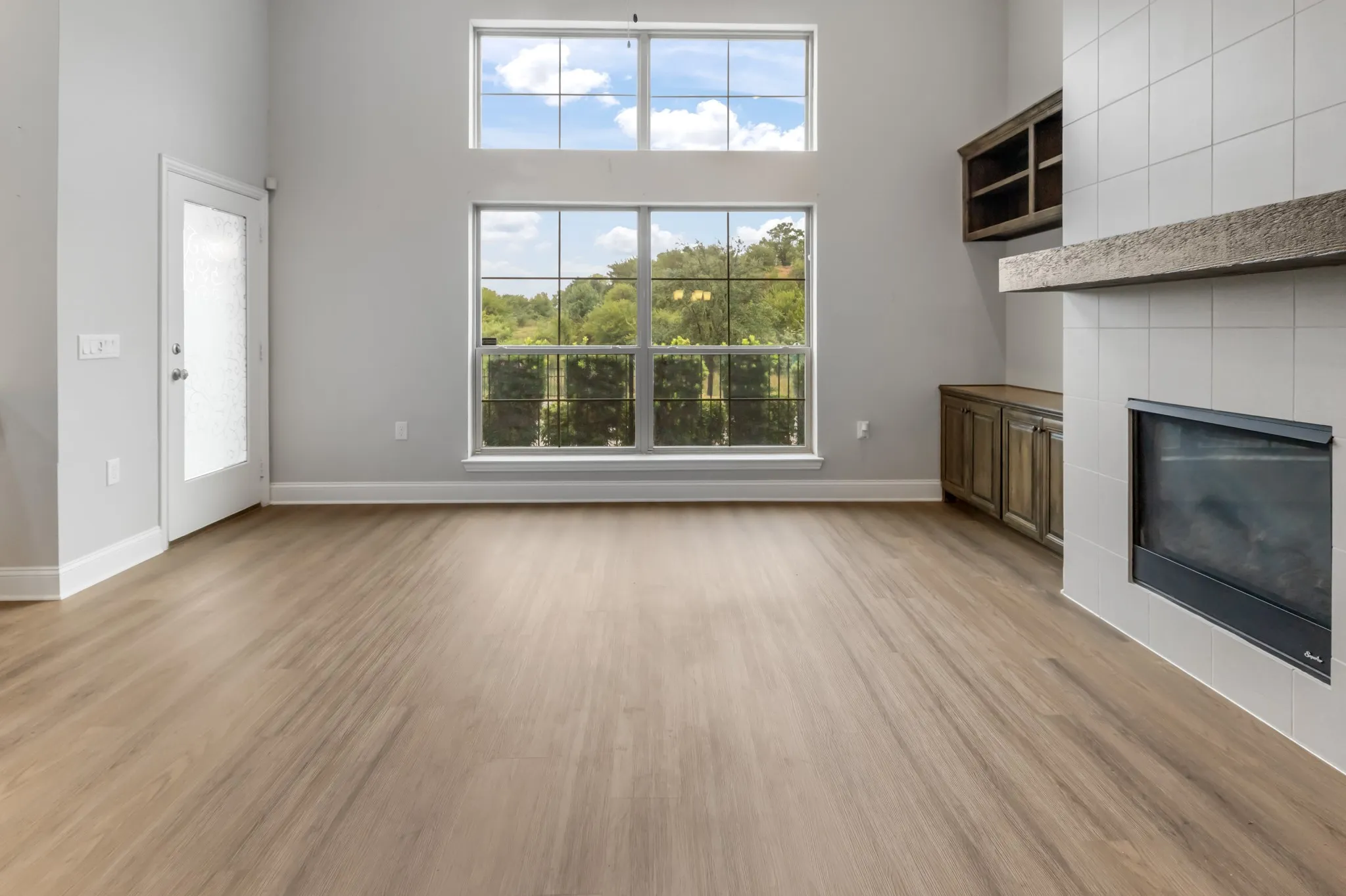 Vaulted ceiling with transom windows, wood-finish flooring, tiled fireplace with a wood mantle, and built-in cabinetry