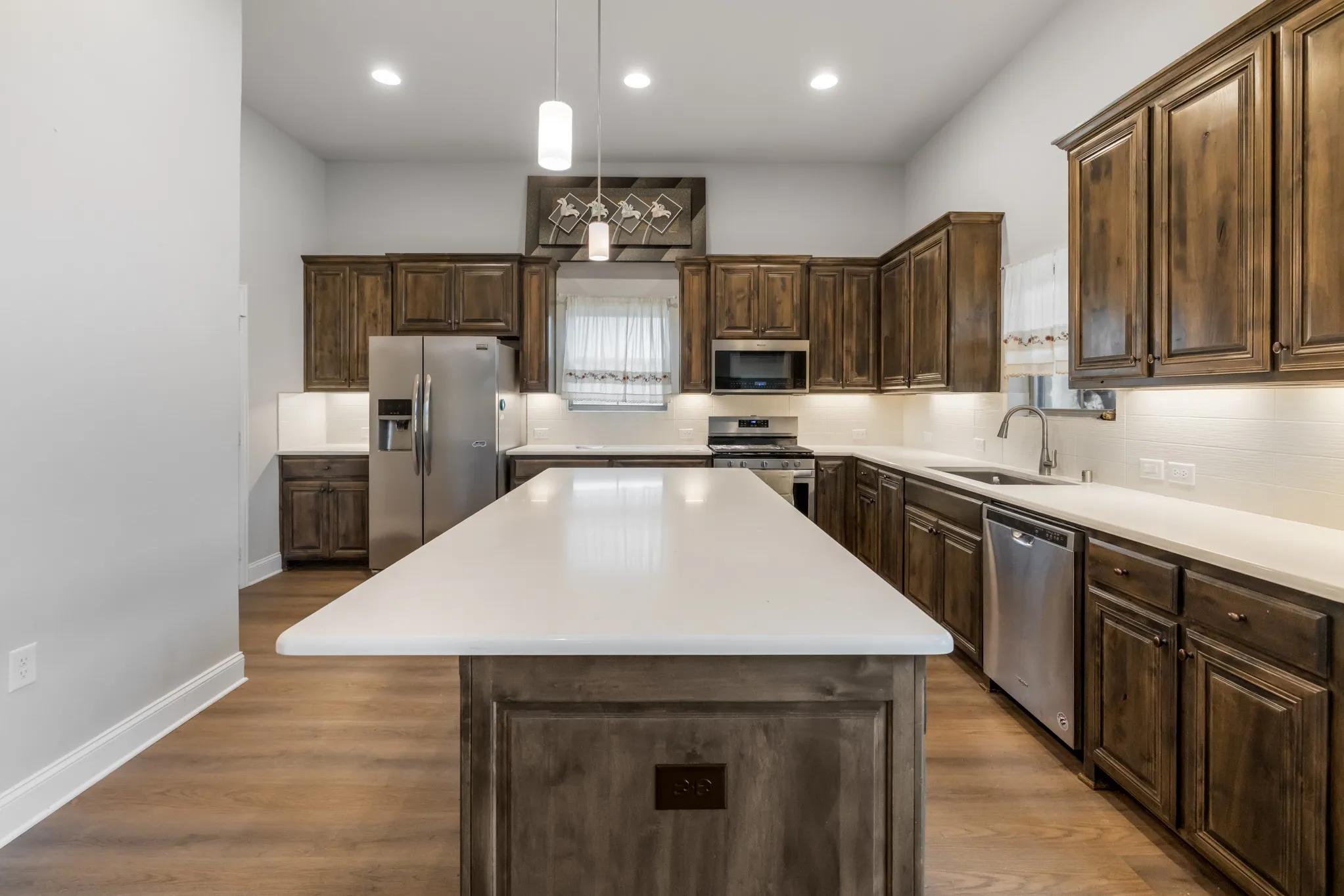 Kitchen featuring wood-finish flooring, dark wood cabinetry, white countertops, stainless steel appliances, and a central island with pendant lighting