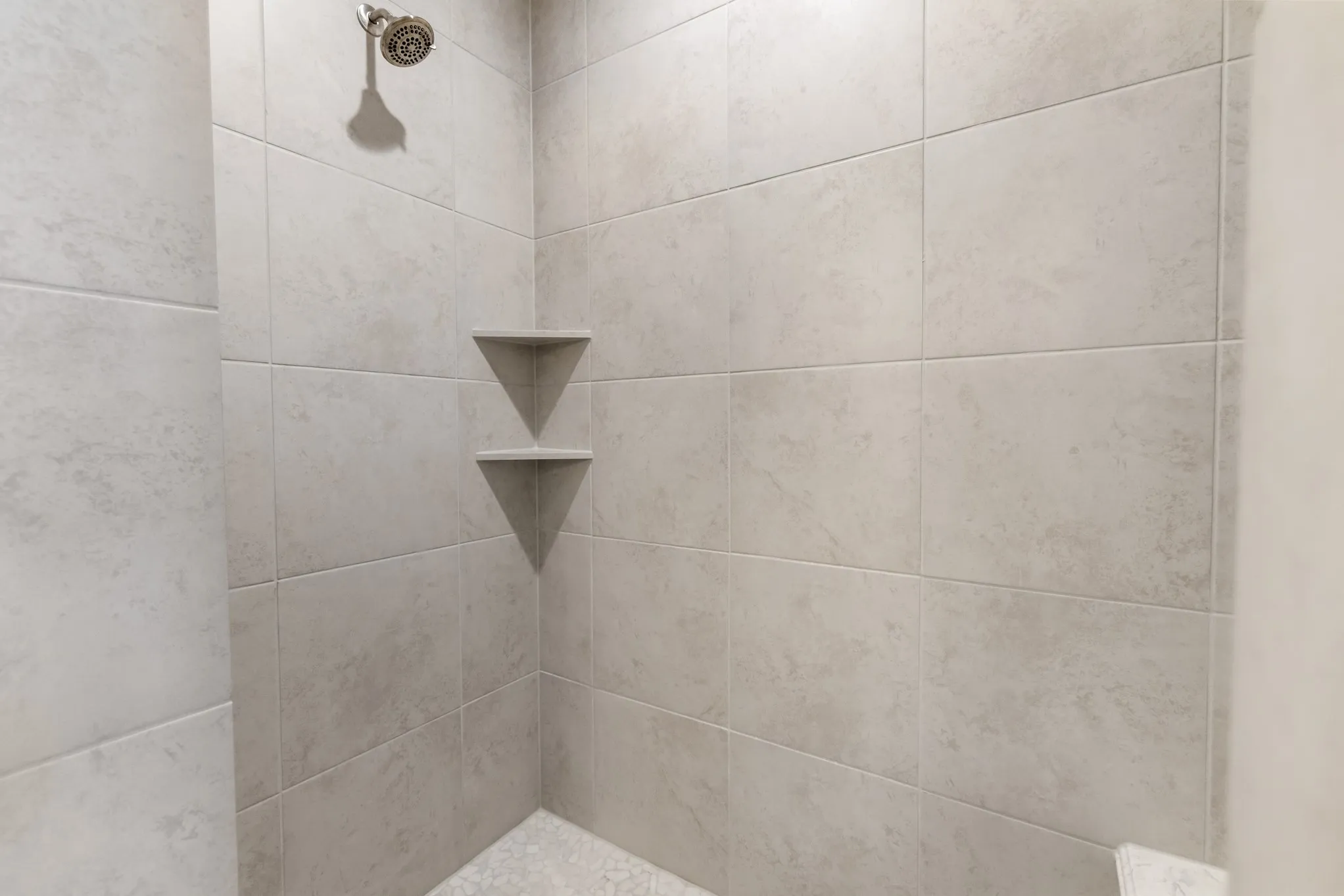 Shower with light-toned wall tiling, two built-in corner shelves, and a textured shower pan