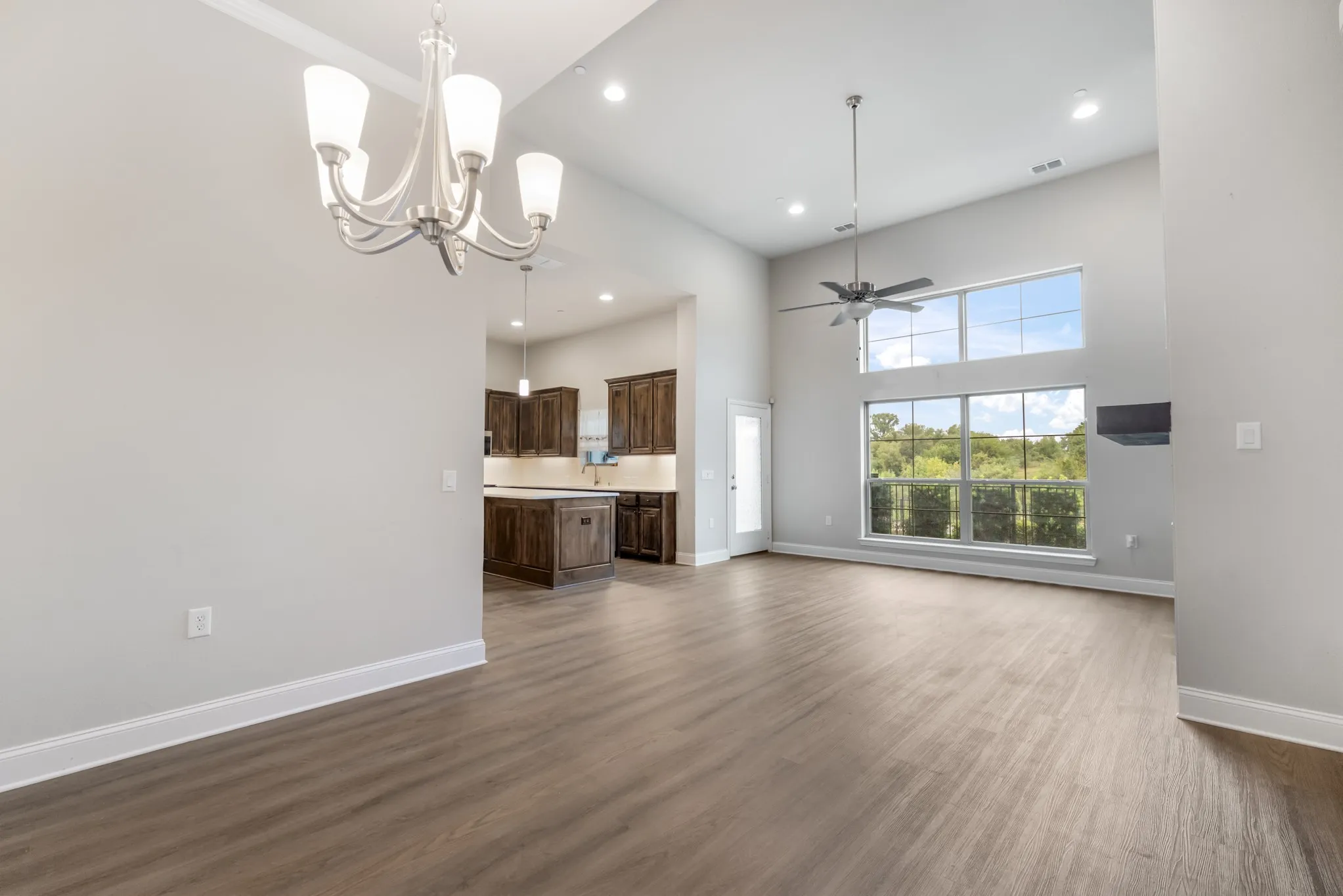 Vaulted ceilings featuring recessed lighting and a ceiling fan, wood-finish flooring, a contemporary chandelier, a kitchen with dark wood cabinetry, and extensive windows