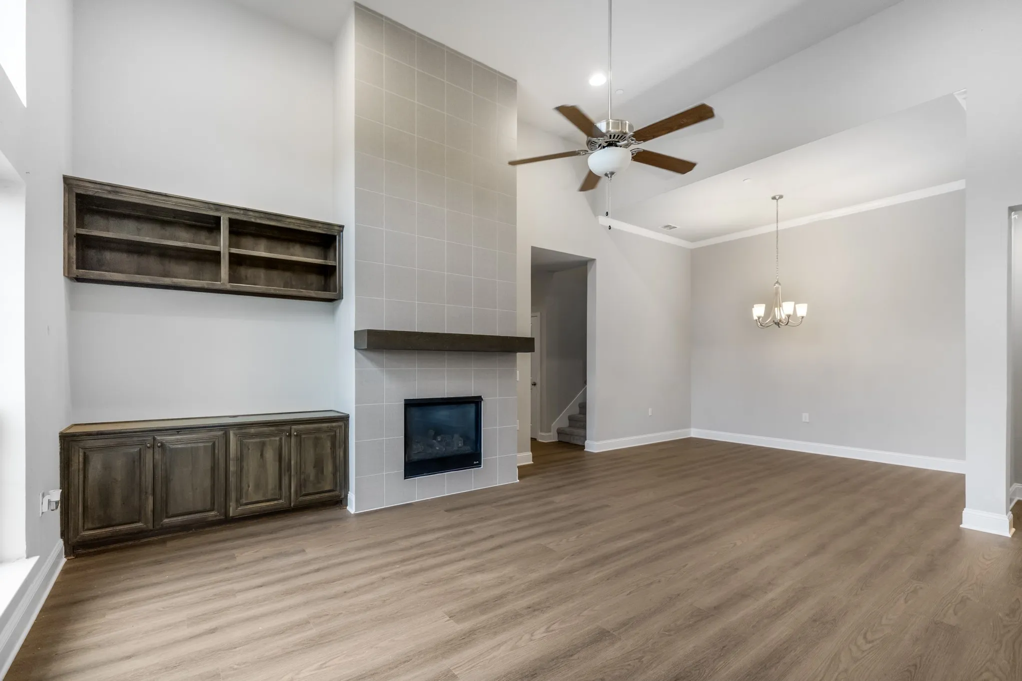 Vaulted ceiling with a ceiling fan, tiled fireplace with a wood-finish mantel, built-in wood-finish shelving and cabinetry, and wood-finish flooring