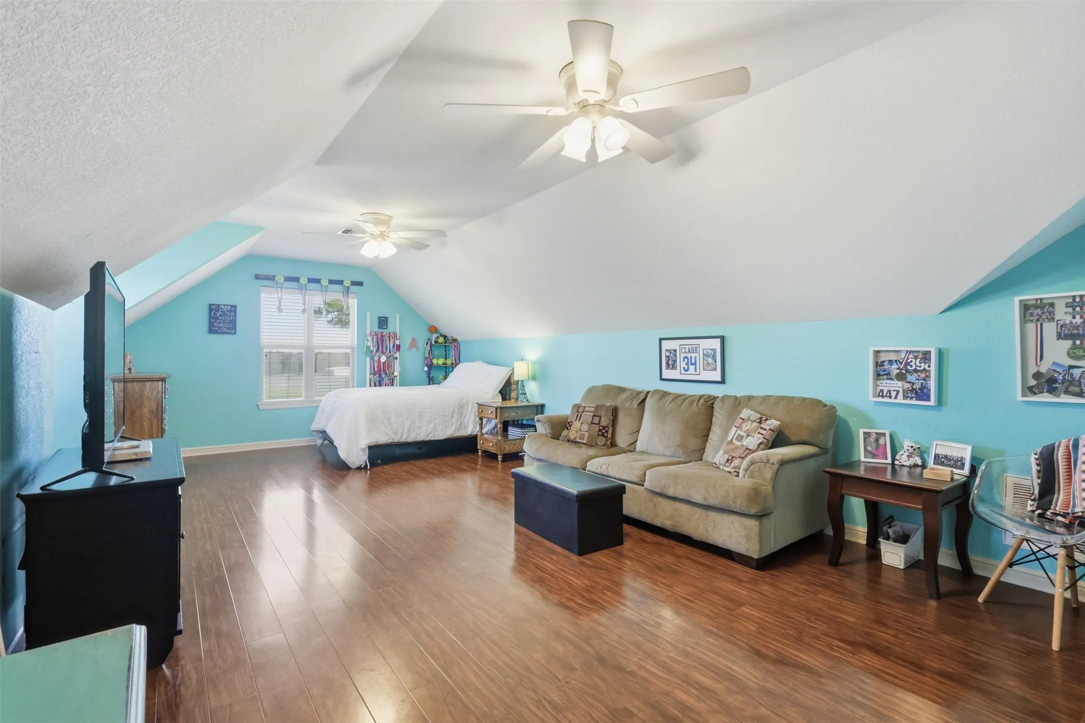 Sloped ceilings, wood-finish flooring, two ceiling fans with integrated lighting, and a double window