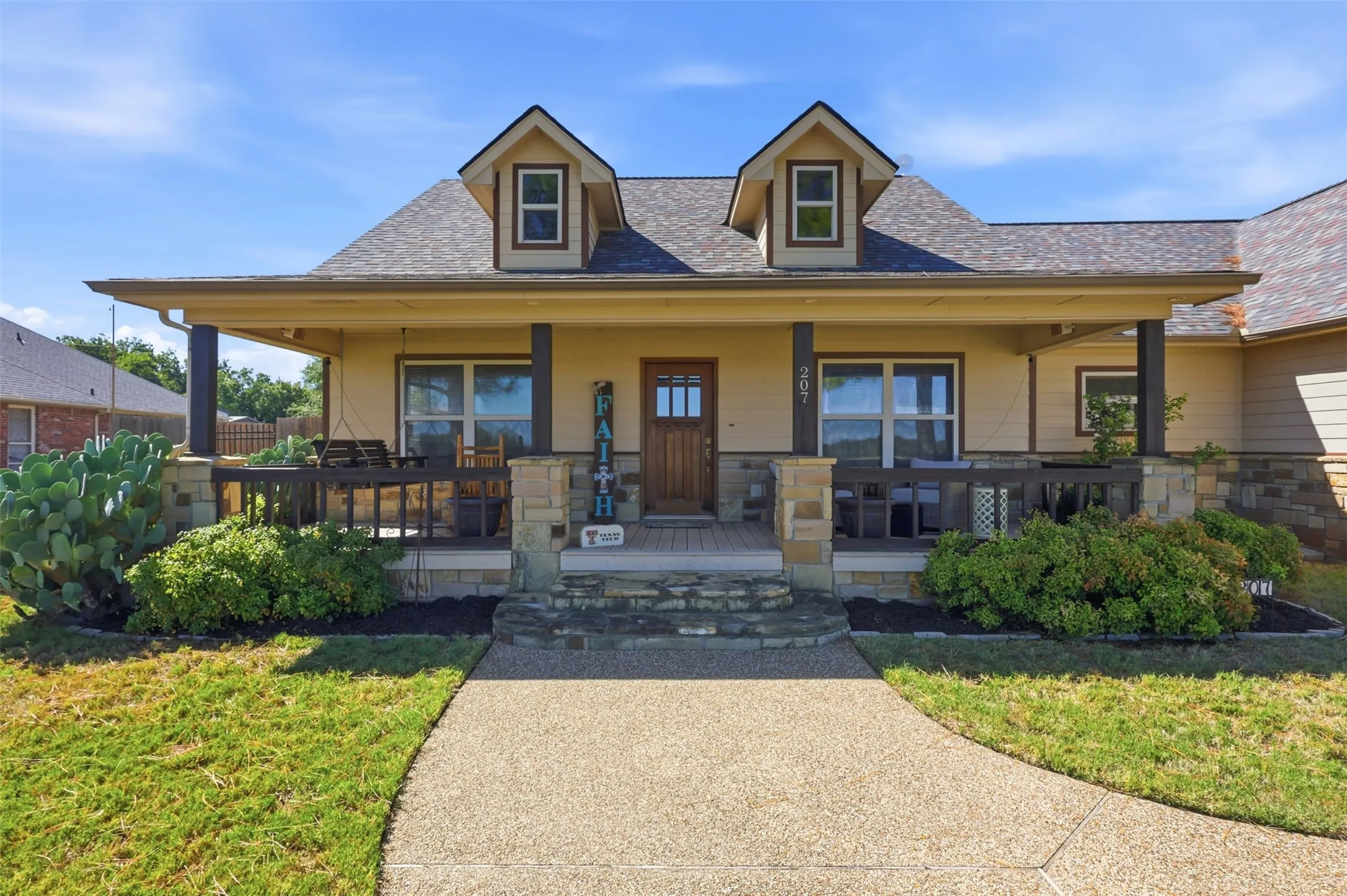 Front exterior with a covered porch, dormer windows, and a stone-clad foundation