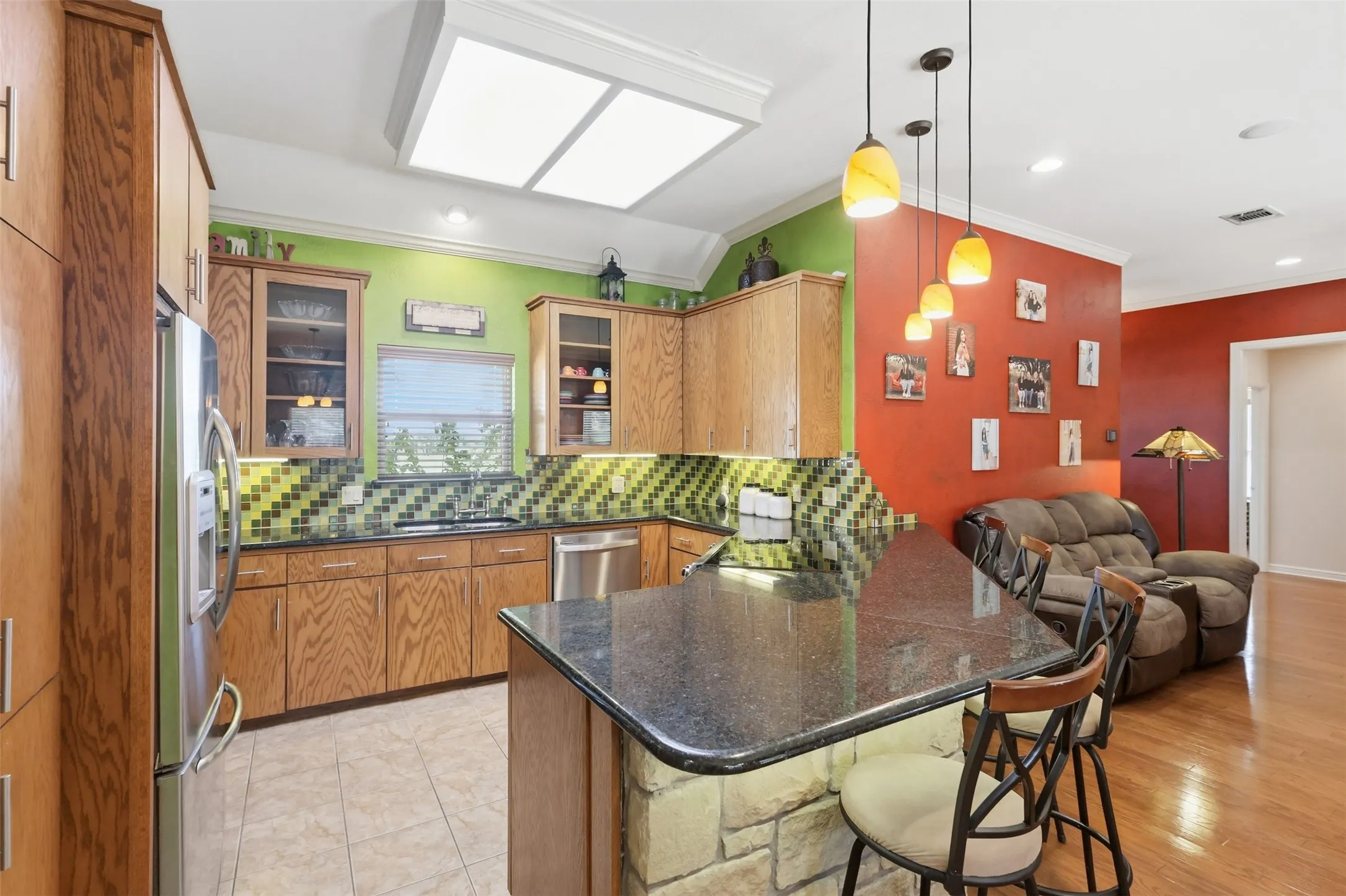 Kitchen featuring wood cabinetry, stainless steel appliances, a black countertop island with stone base, and pendant lighting