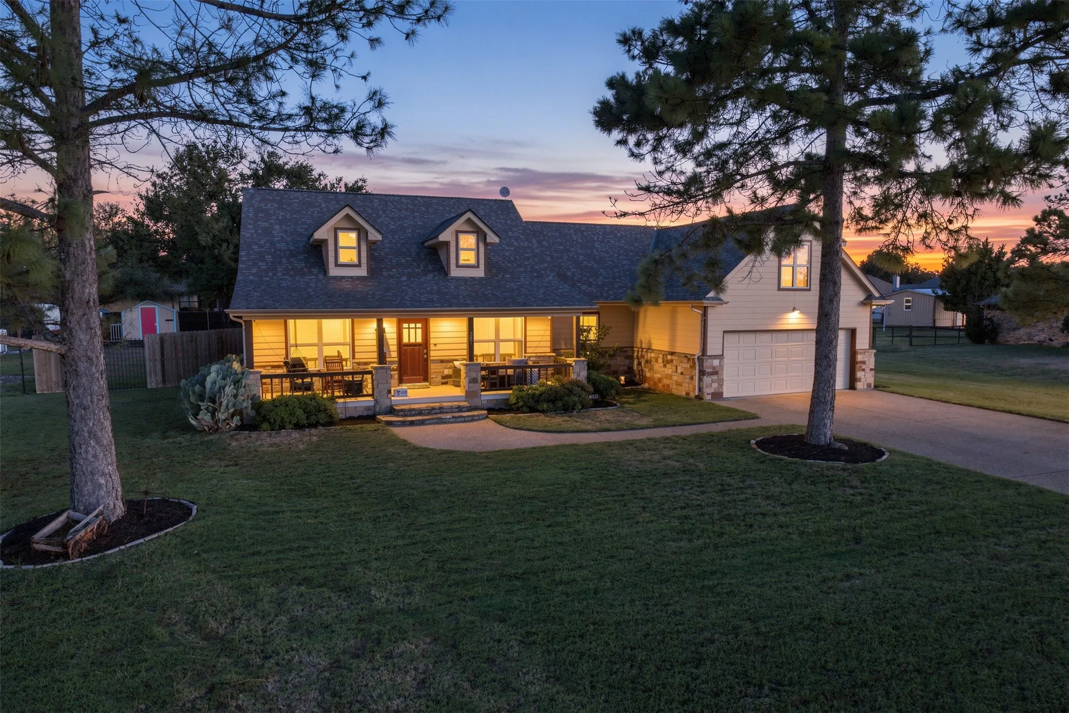 Gable roofline with dormer windows, stone accent siding, covered front porch, attached garage, and paved driveway