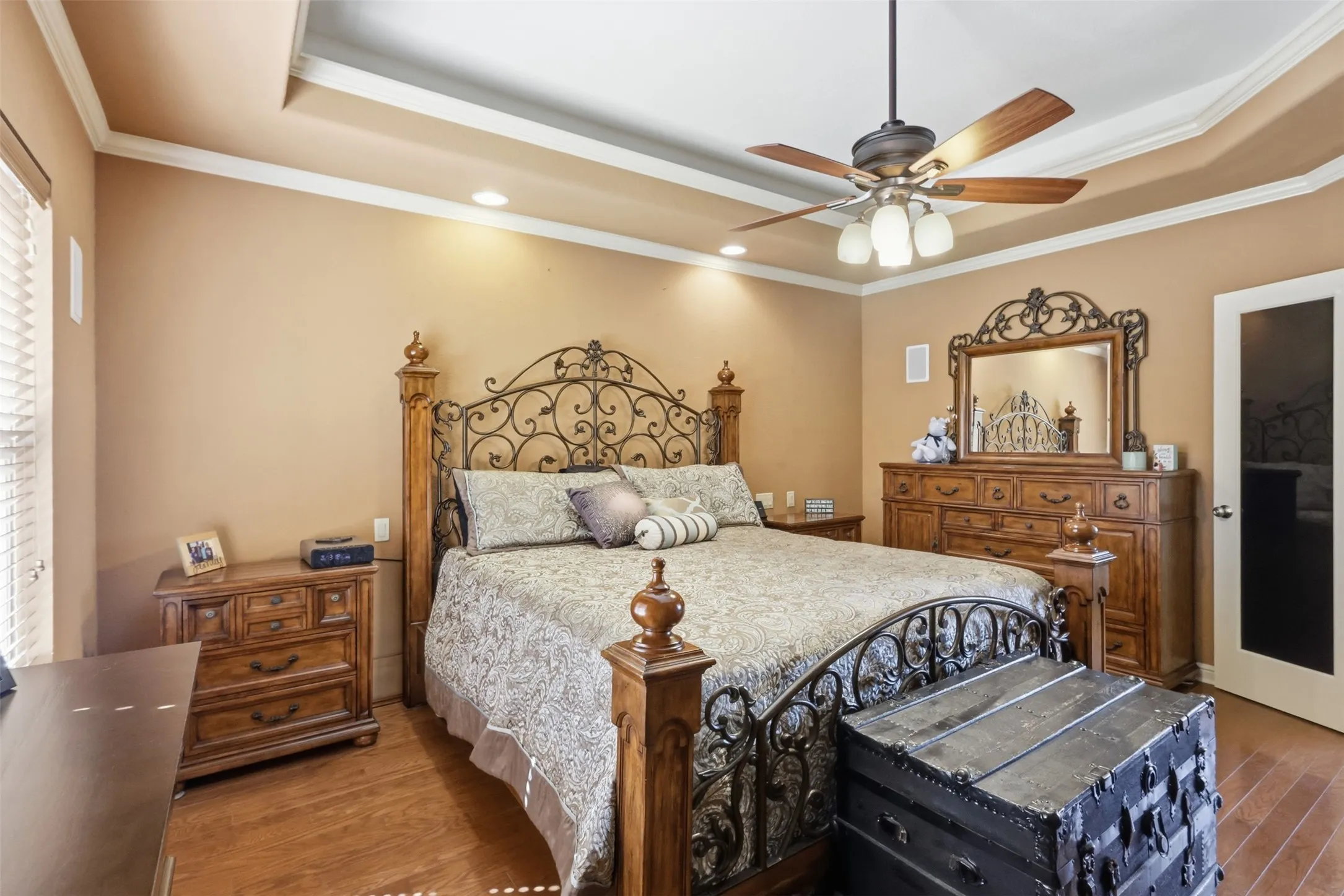 Tray ceiling with crown molding, recessed lighting, wood-finish flooring, and a ceiling fan with integrated lighting