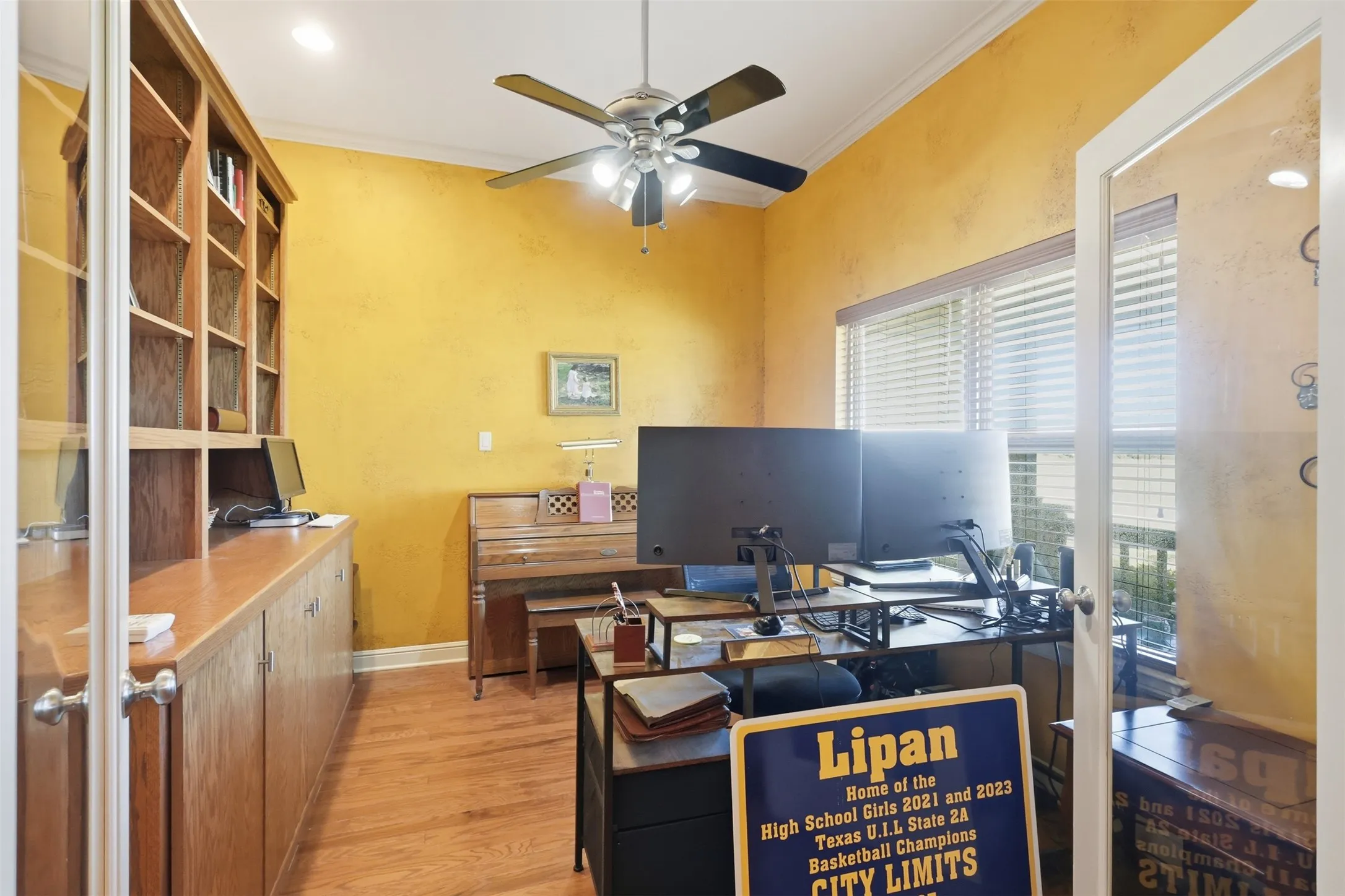 Wood-finish flooring, built-in shelving, glass-panel French doors, ceiling fan with integrated lighting, and crown molding