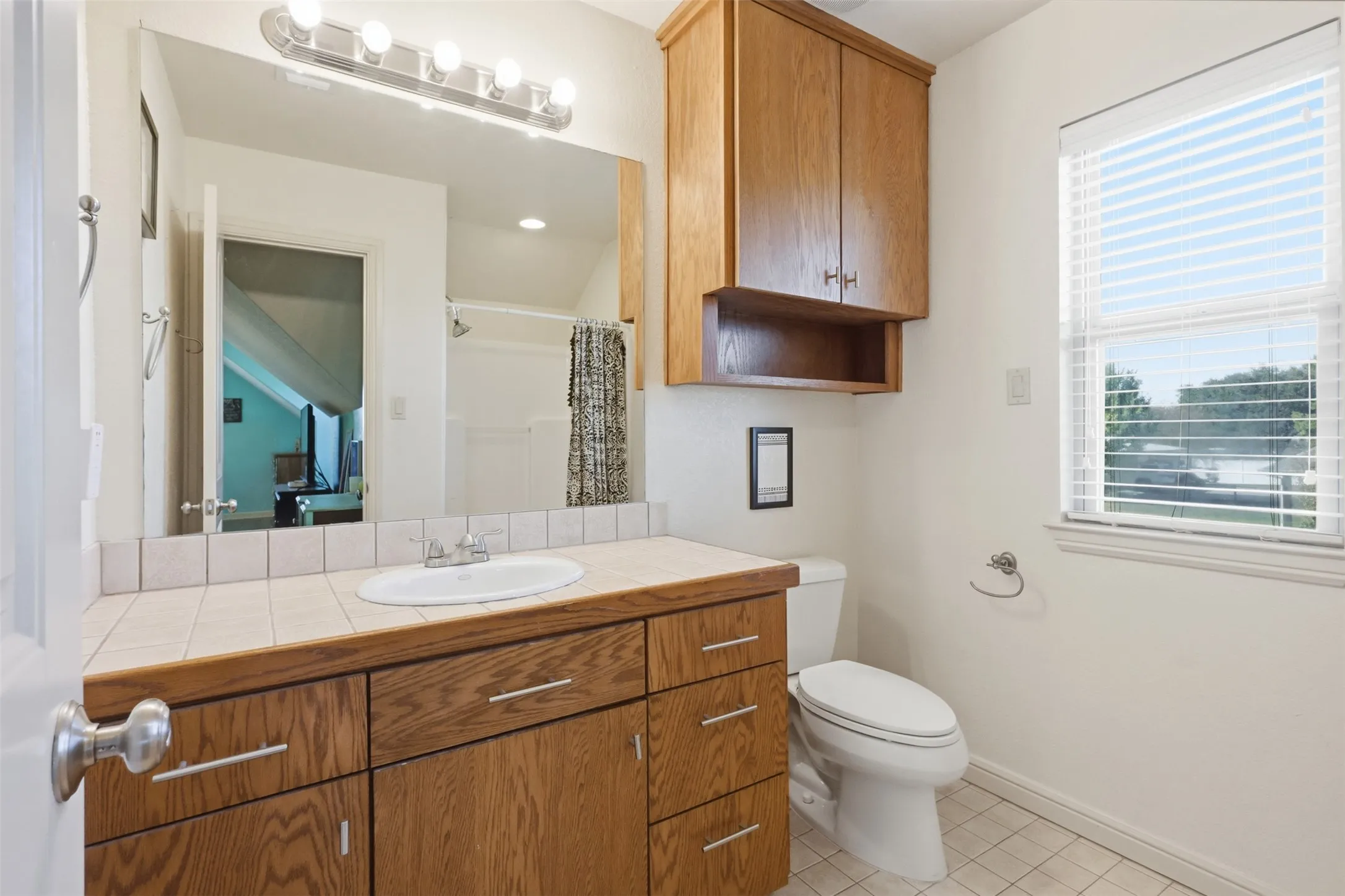 Bathroom featuring a single vanity with wood-finish cabinetry, a tiled countertop, and an integrated sink