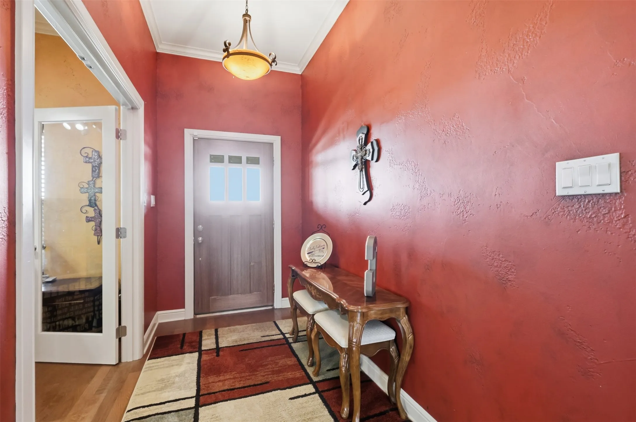 Vaulted entryway with wood-finish flooring, decorative ceiling light fixture, and wood-paneled door with glass inserts