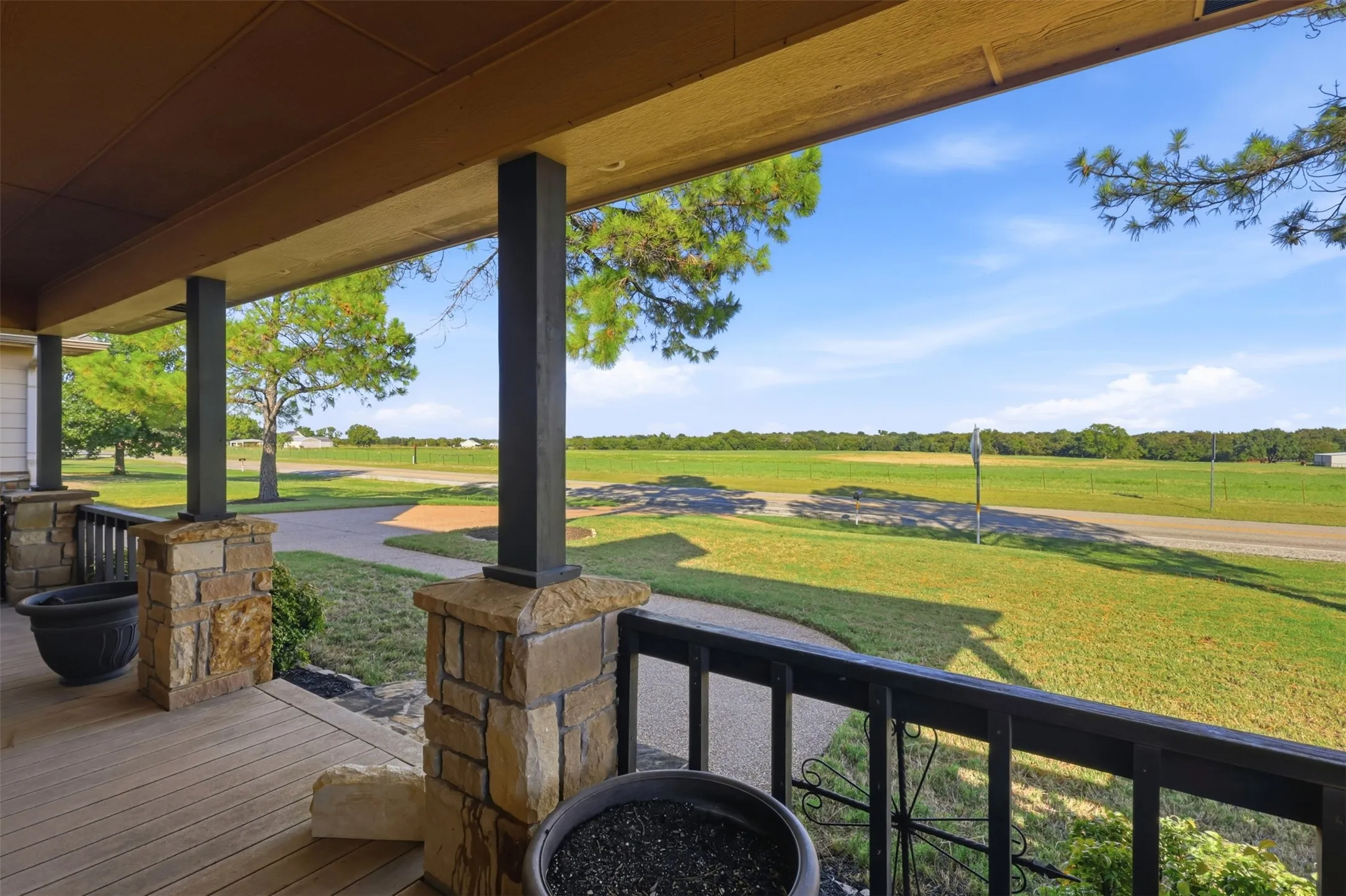 Covered porch with wood-finish decking, stone-clad pillars, and wrought iron railing
