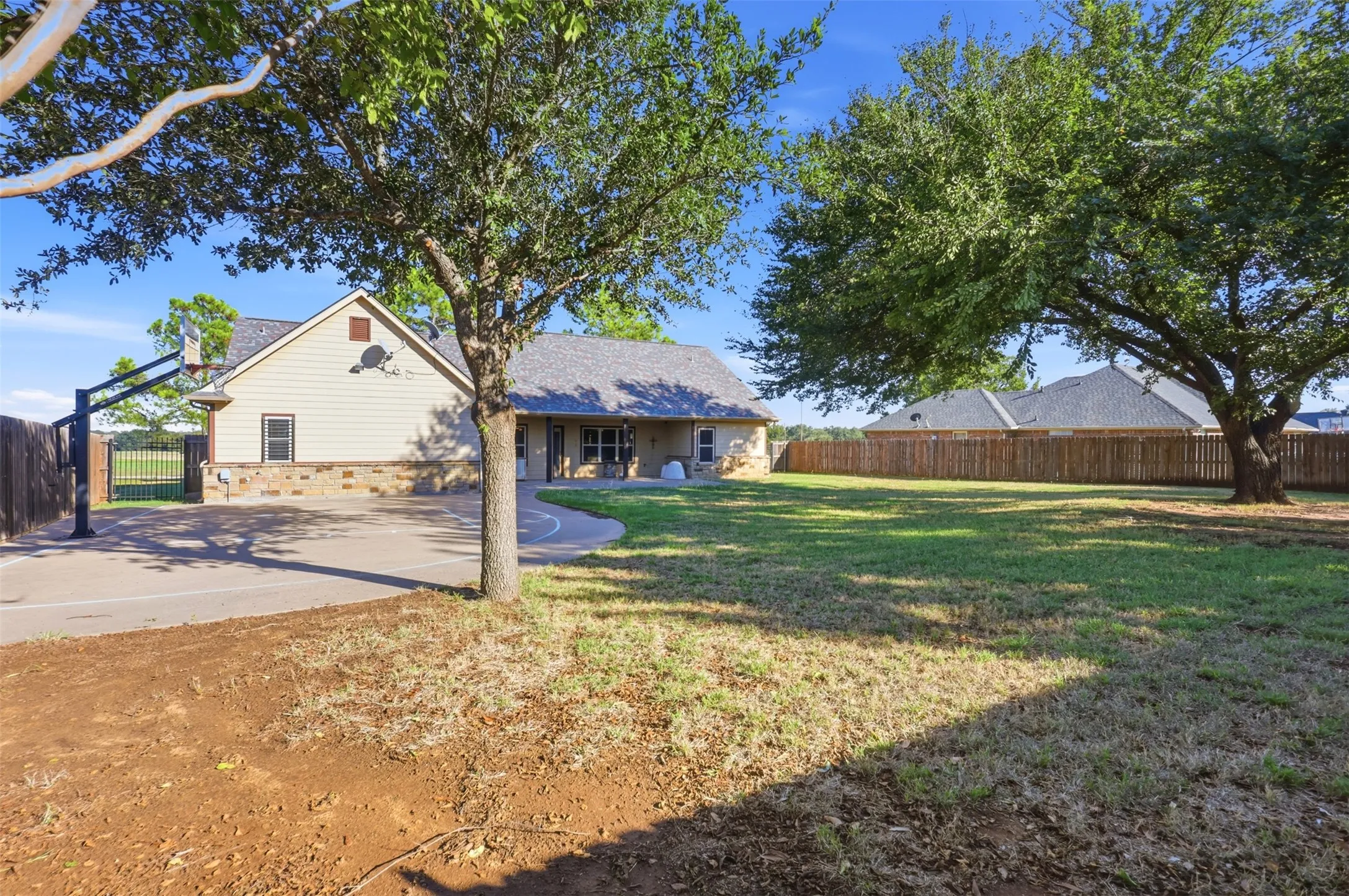 Expansive backyard with a manicured lawn, mature trees, wood fence, and a paved sport court