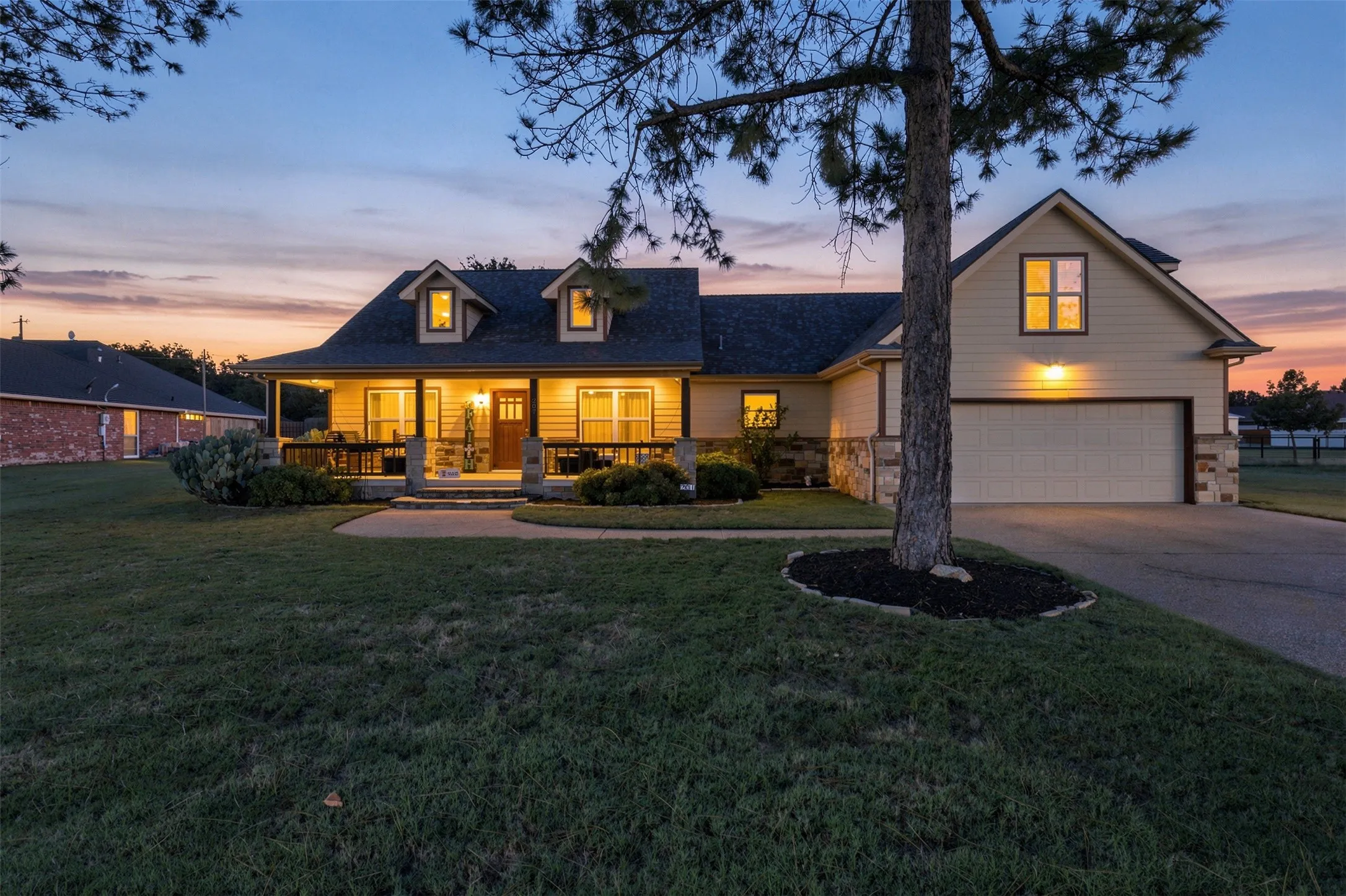 Craftsman-style home with dormer windows, stone accents, a covered front porch, and an attached two-car garage