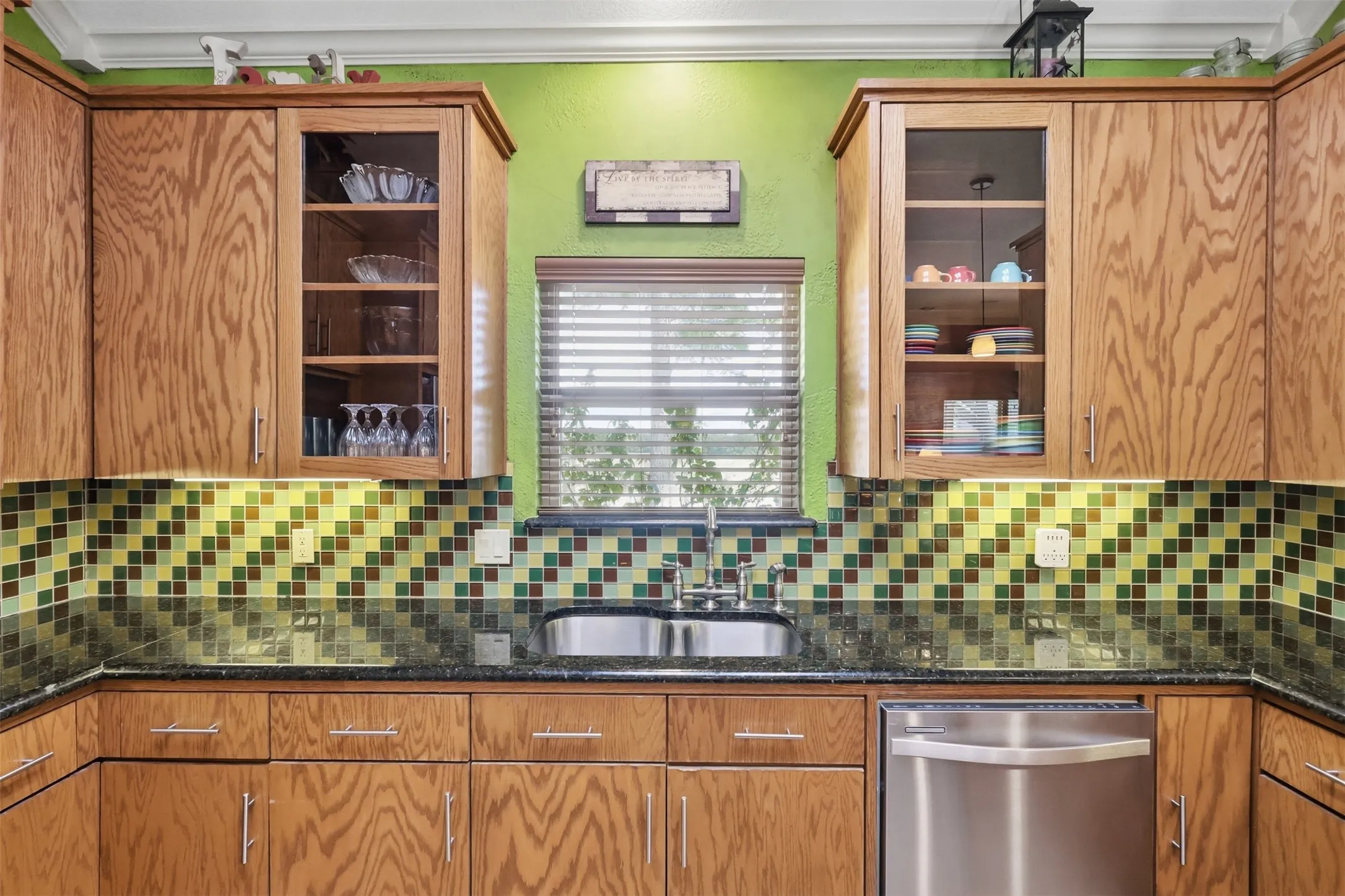 Wood-finish cabinetry with glass-front uppers, stainless steel sink, tiled backsplash, and stainless steel dishwasher