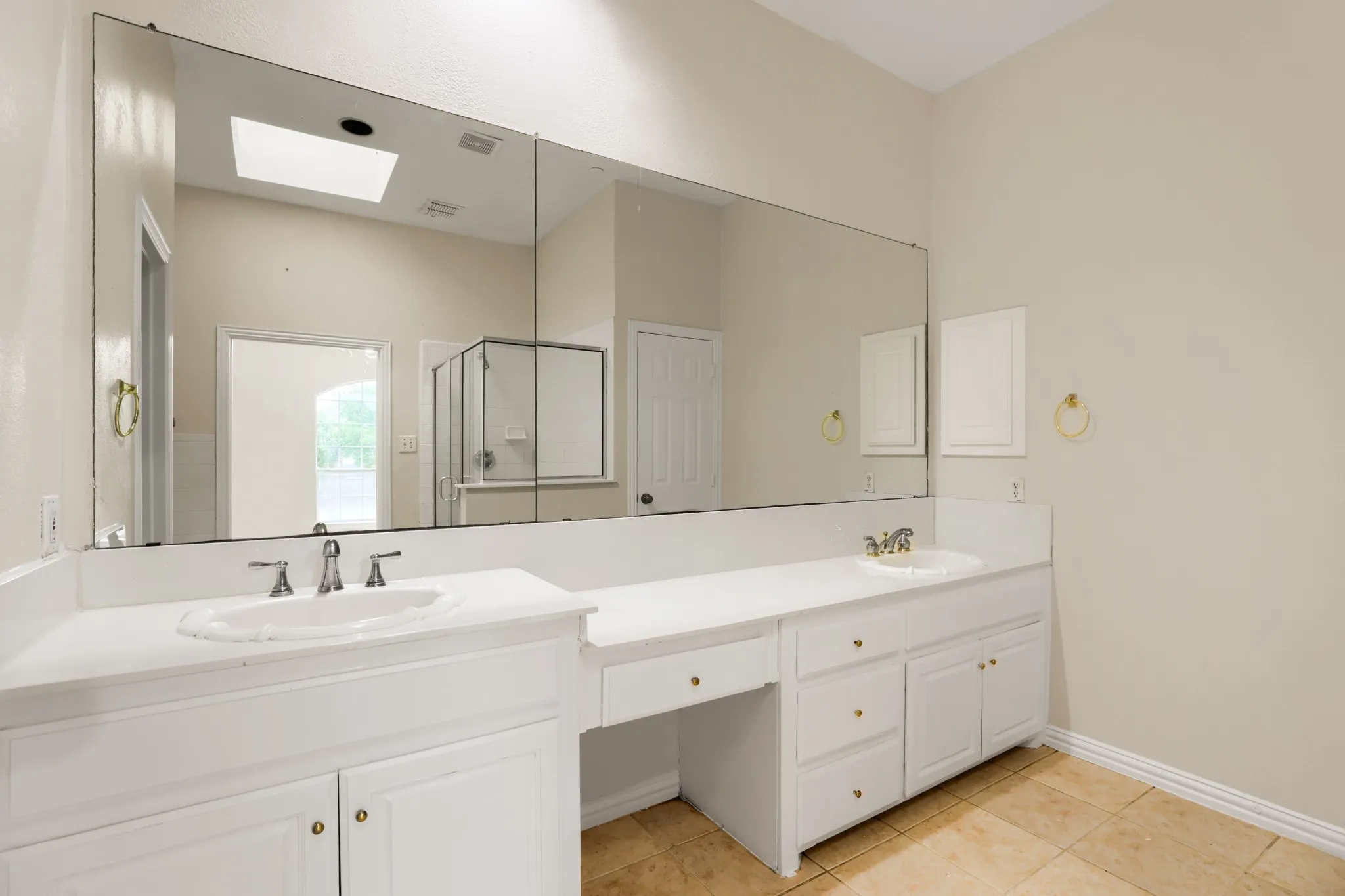 Dual vanity sinks with white cabinetry, a built-in vanity area, and a skylight