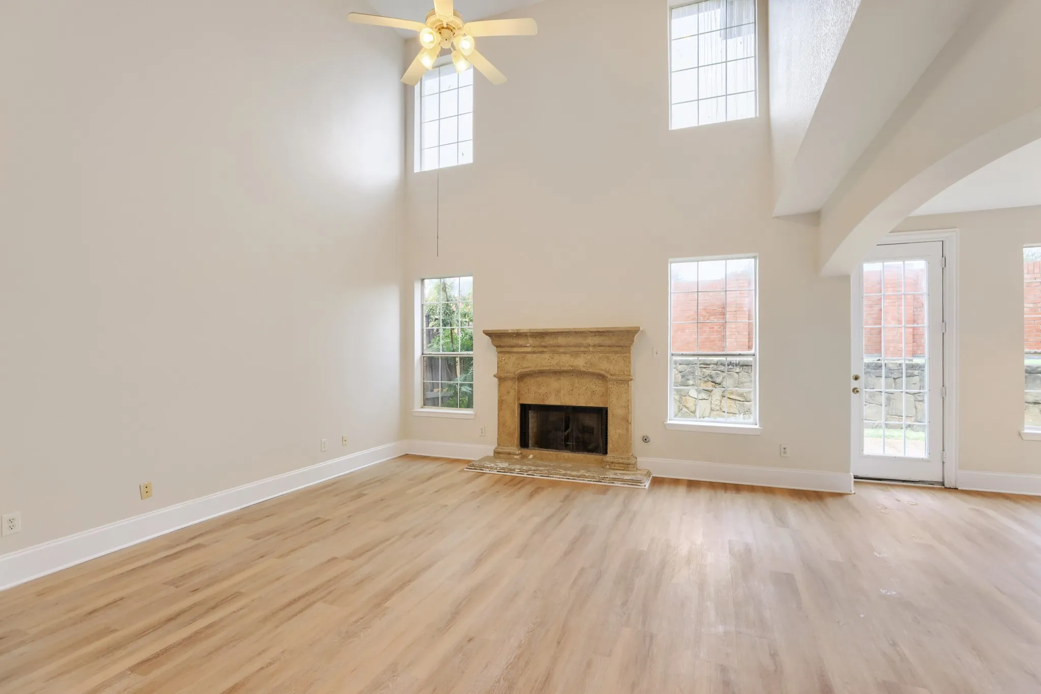 Two-story living space featuring a fireplace with stone surround, wood-finish flooring, high ceilings, and multiple windows