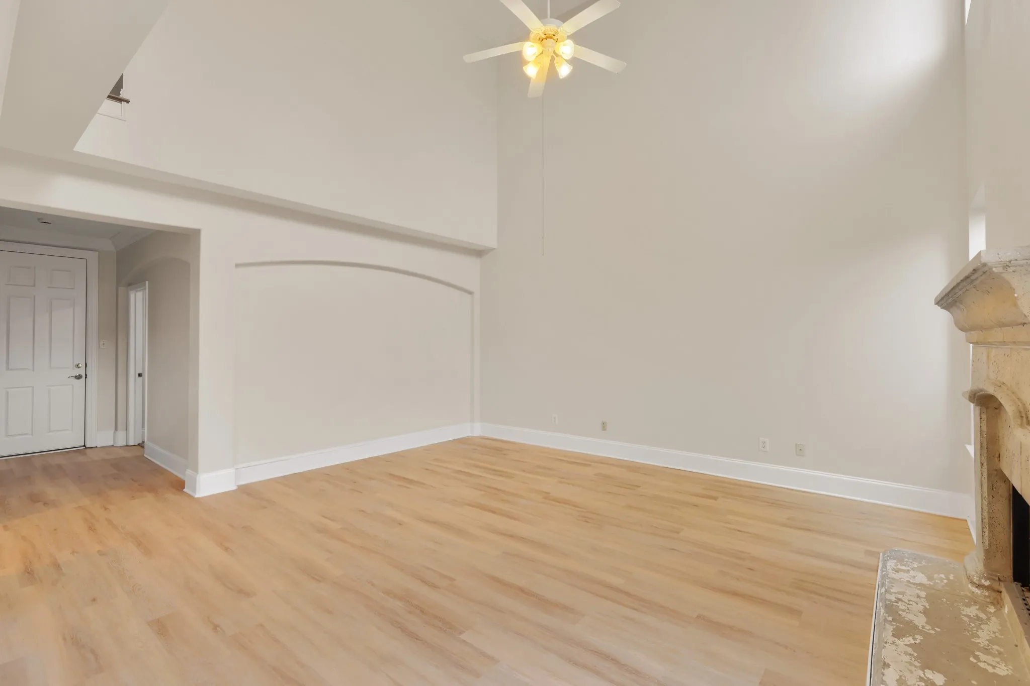 Vaulted ceiling with a ceiling fan, wood-finish flooring, stone-clad fireplace, and an arched wall detail