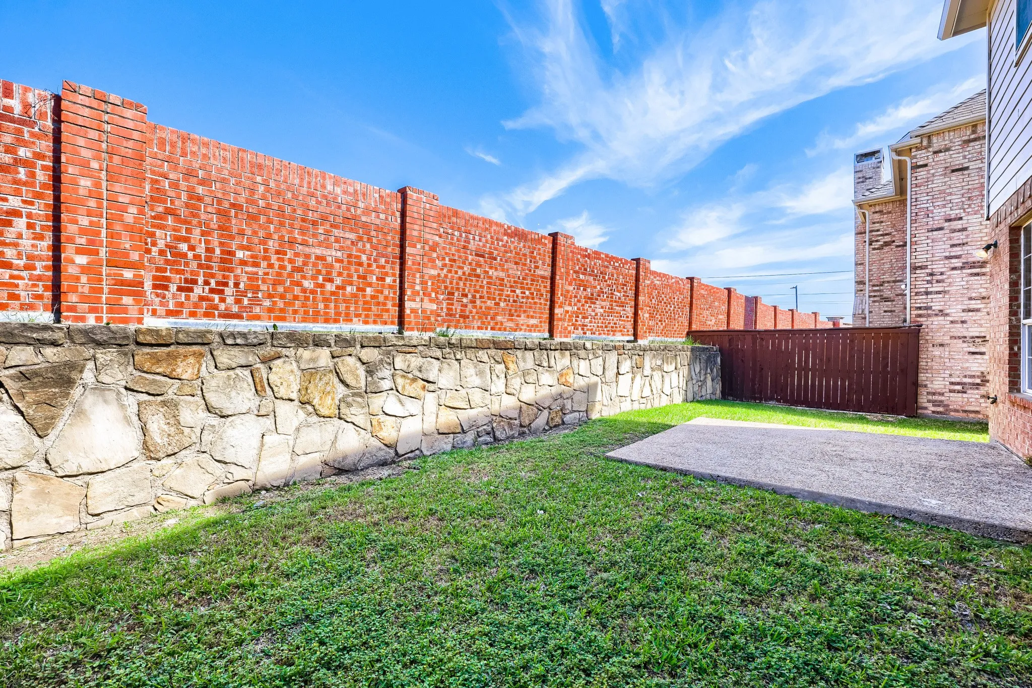 Private backyard featuring a concrete patio, a stone and brick privacy wall, and a wood privacy fence