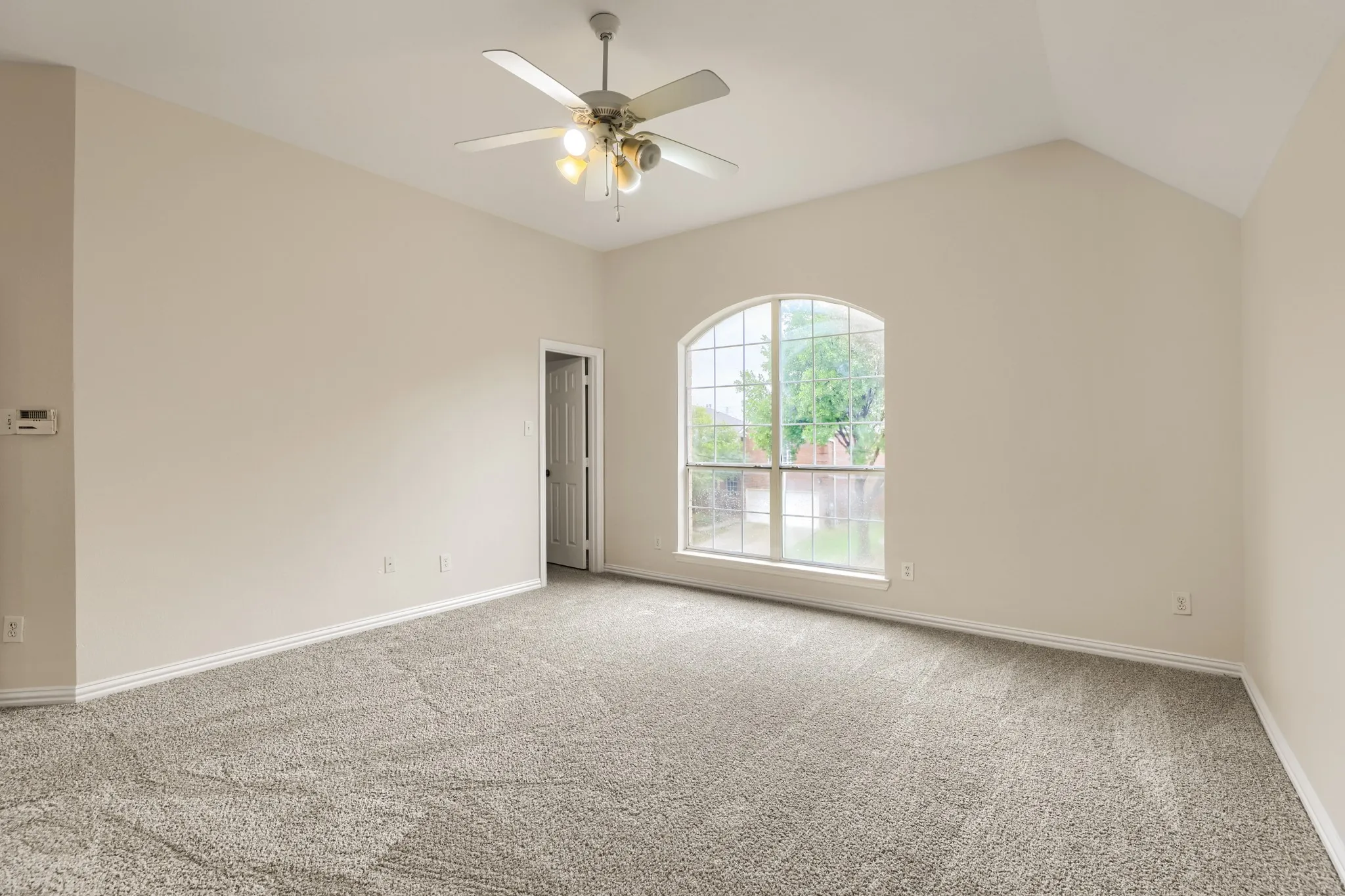 Arched window, vaulted ceiling, ceiling fan with integrated lighting, wall-to-wall carpeting, and light-toned walls
