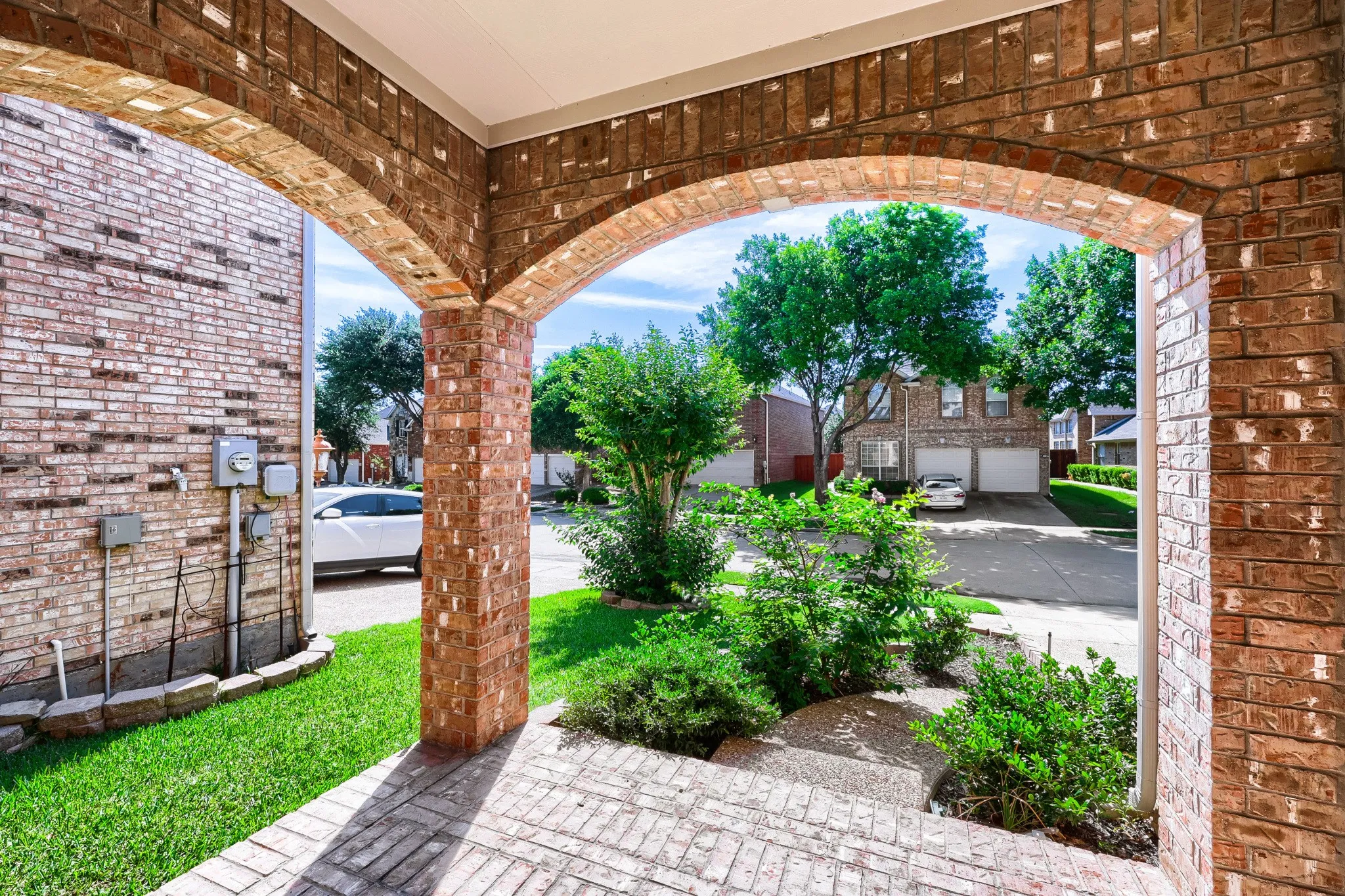 Brick archways and columns, brick flooring, landscaped shrubbery, and a manicured lawn