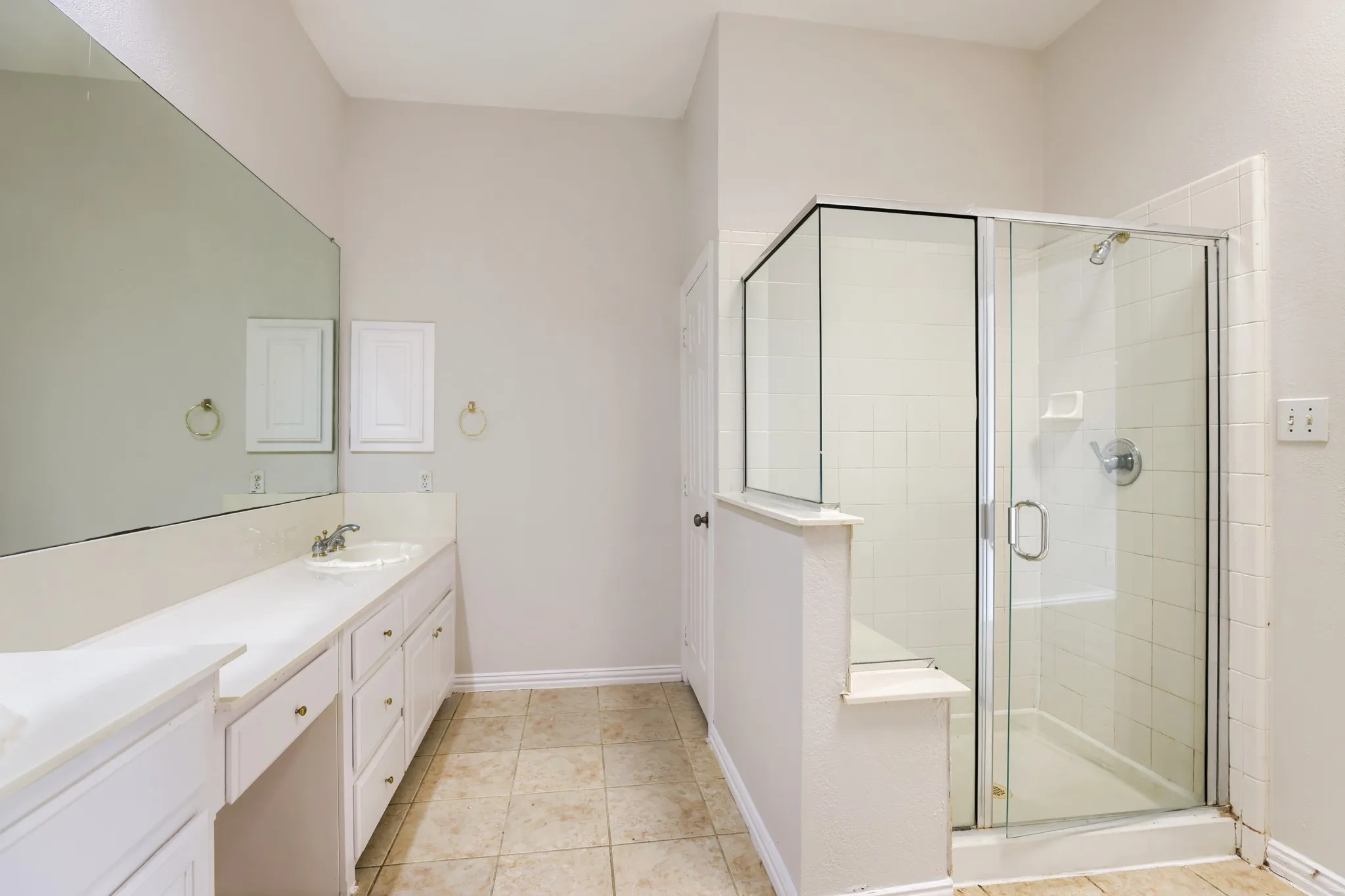 Extended vanity with integrated sink, full-width mirror, tile flooring, and a glass-enclosed shower