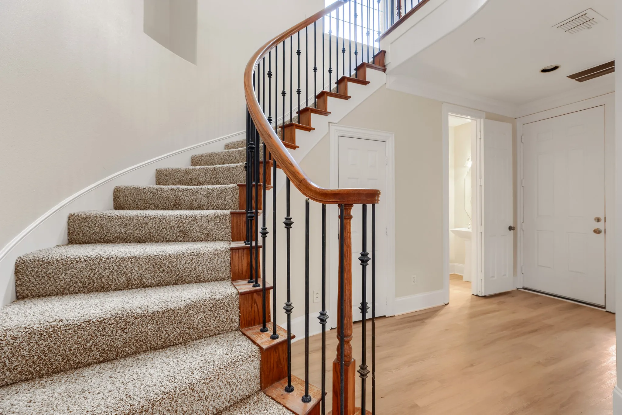 Curved staircase with wood railing, wrought iron balusters, and carpeted treads