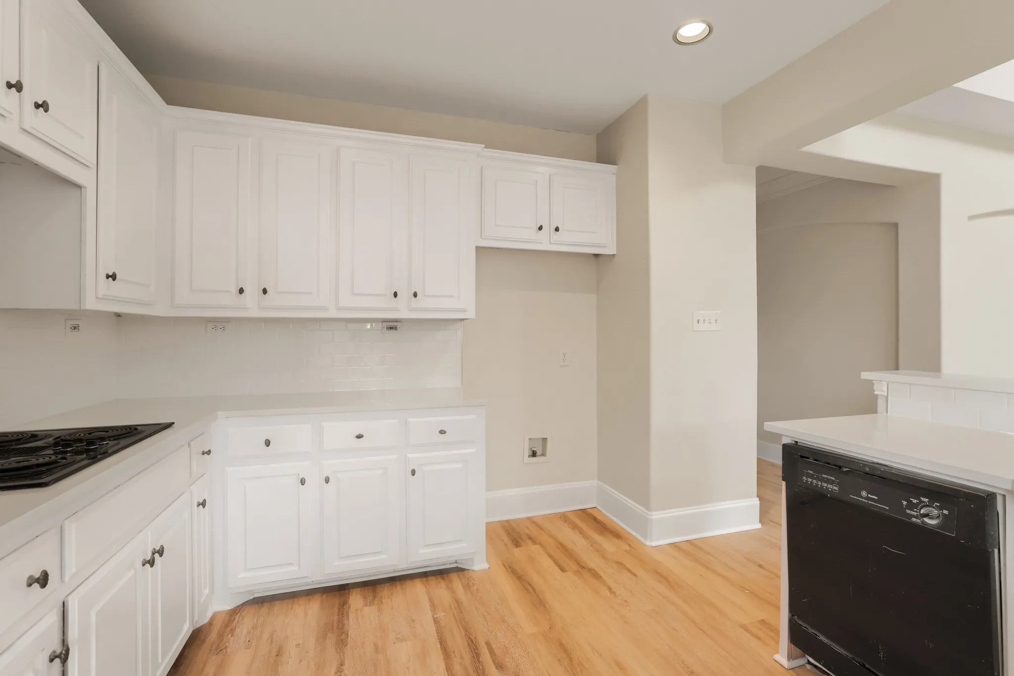 White cabinetry, light-toned wood-finish flooring, recessed lighting, white subway tile backsplash, and a built-in cooktop