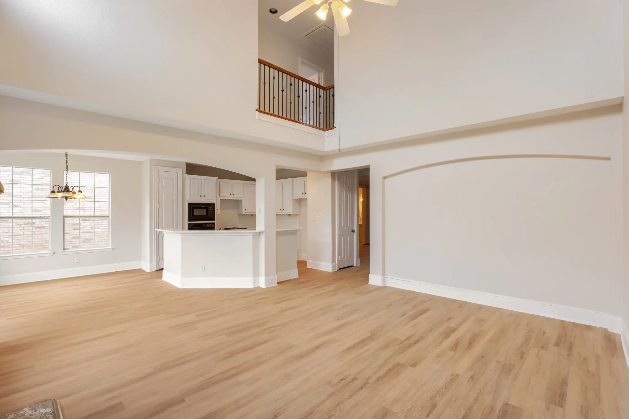 Vaulted ceiling, wood-finish flooring, white cabinetry, built-in microwave, and an interior balcony with wood and wrought iron railing