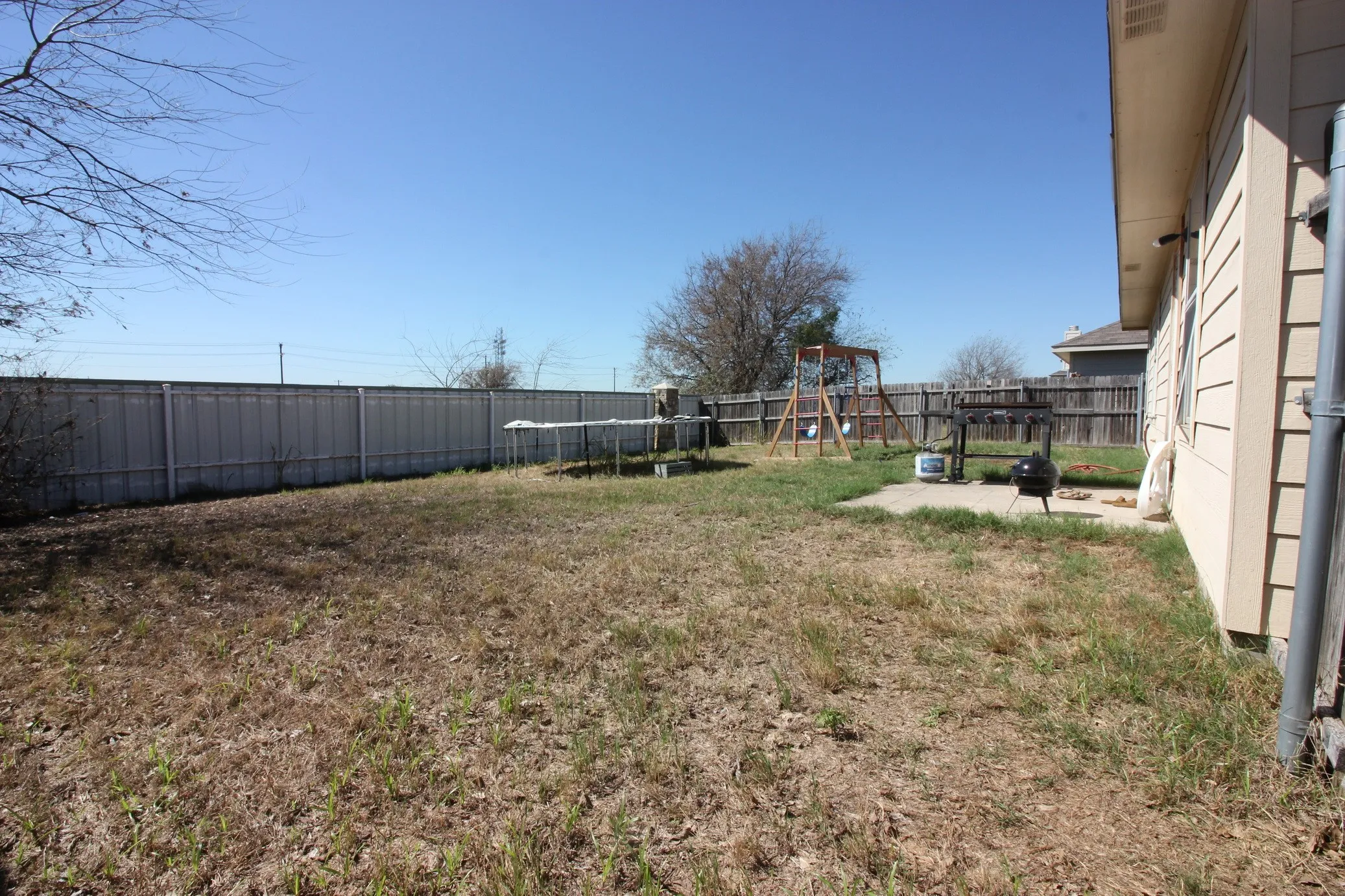Expansive backyard featuring a concrete patio, a full privacy fence, and a wooden swing set