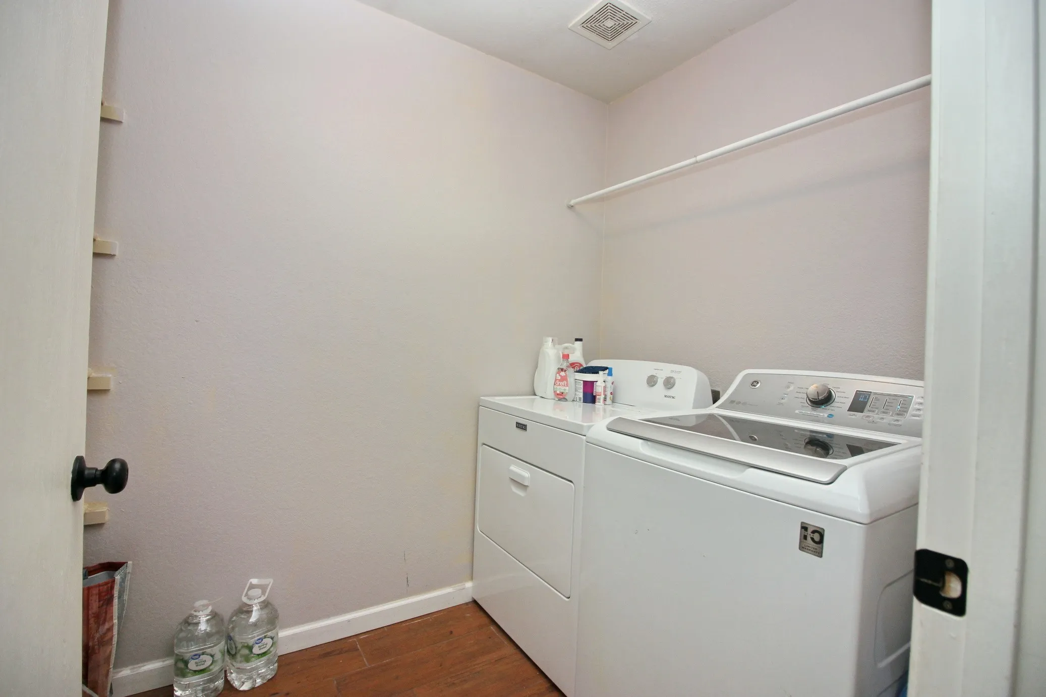 Dedicated laundry space featuring a built-in hanging rod, overhead ventilation, and wood-finish flooring