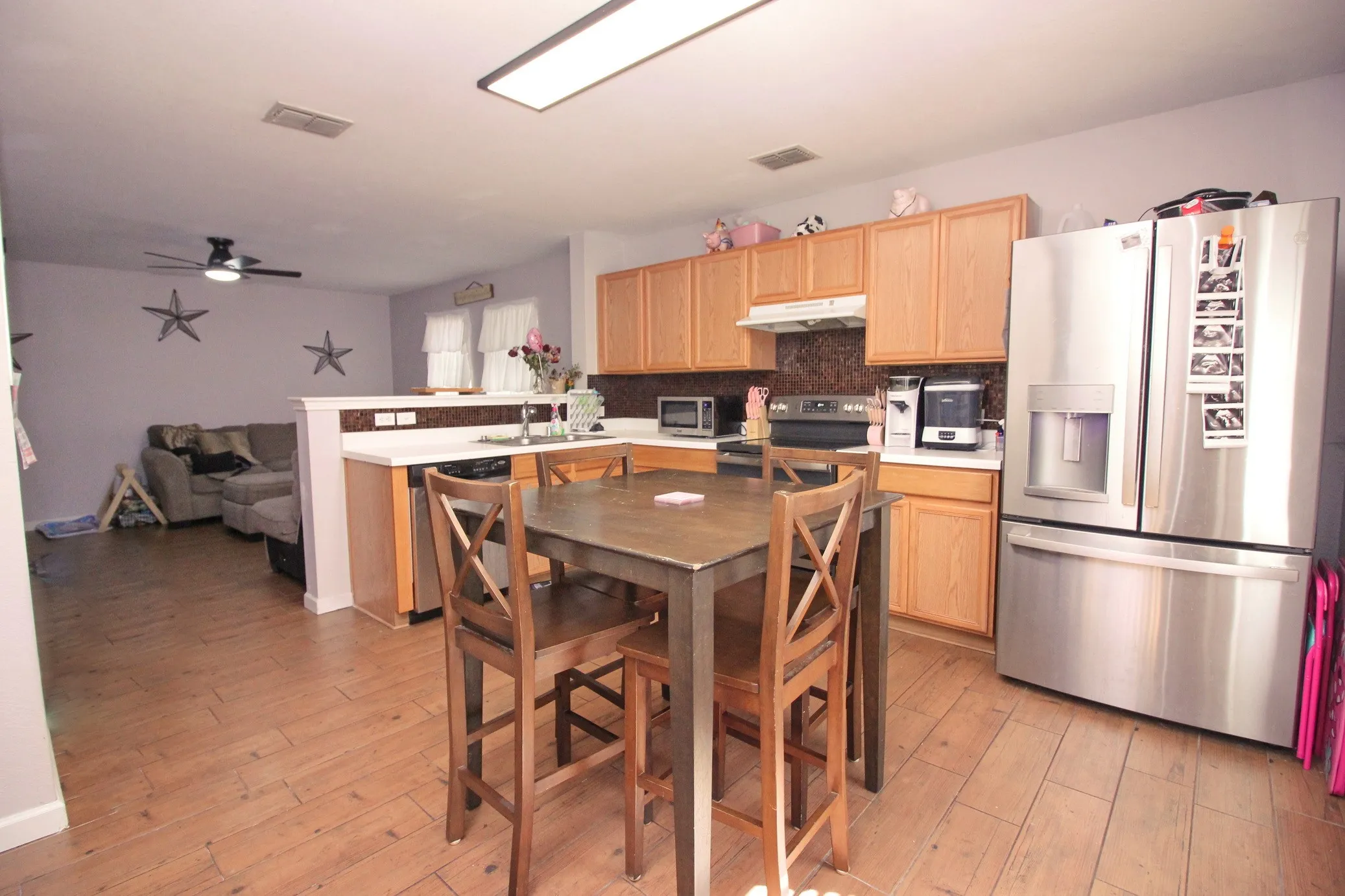 Kitchen featuring wood-finish flooring, stainless steel appliances, light wood cabinetry, and a countertop bar