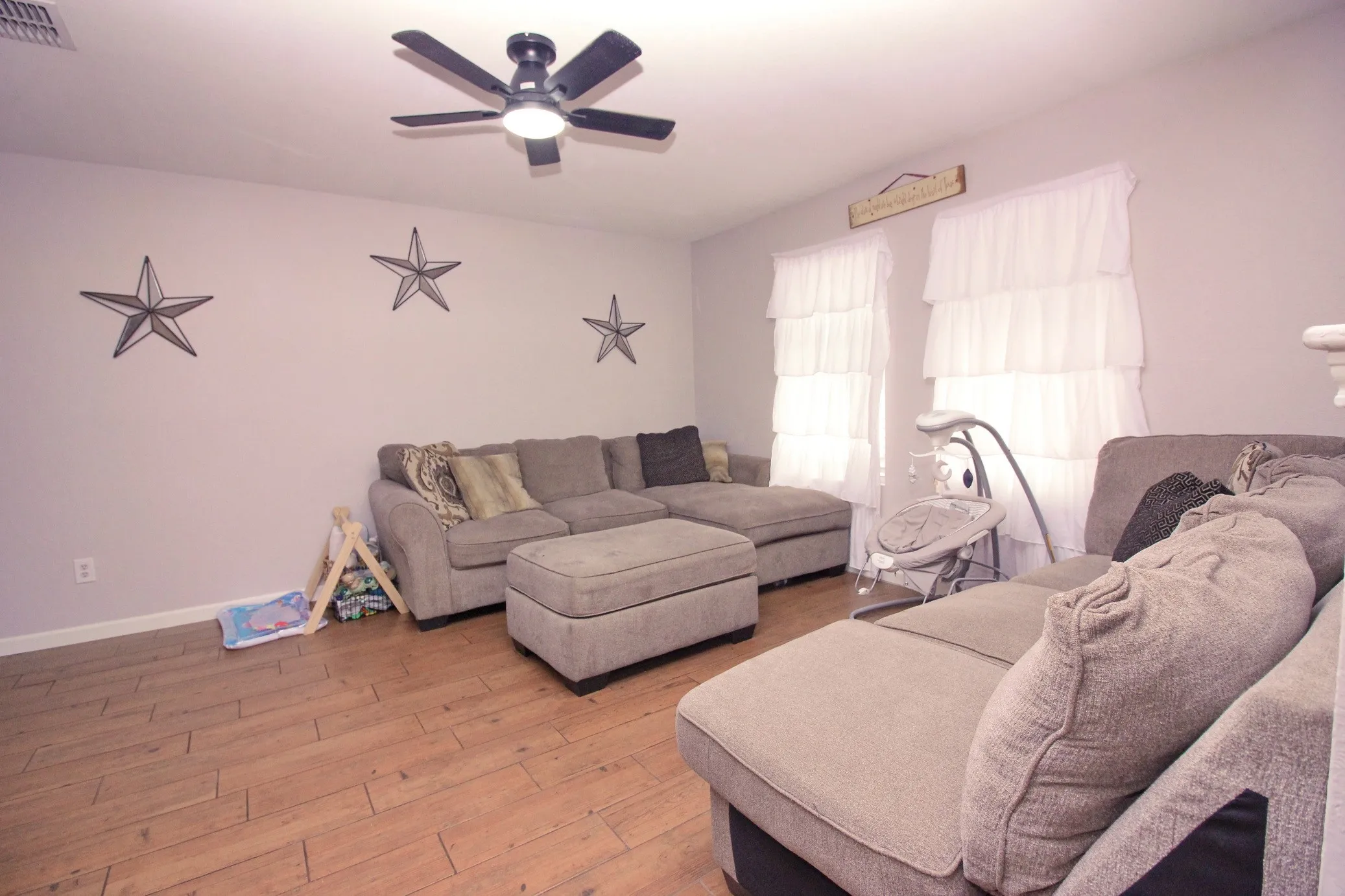 Spacious living area featuring wood-finish flooring, a ceiling fan with integrated lighting, and multiple windows