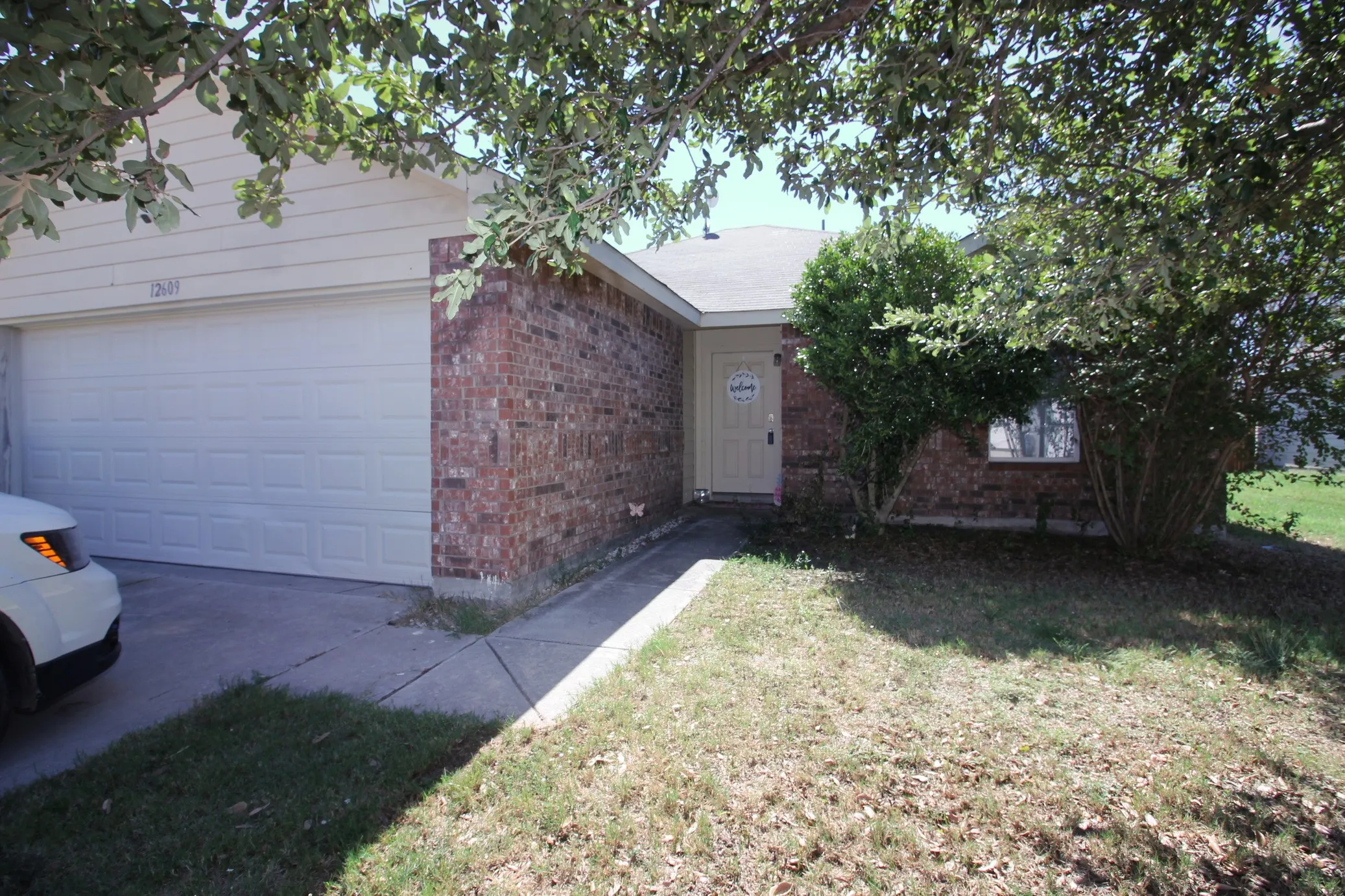 Brick and siding exterior with an attached garage, a paved driveway, and mature landscaping