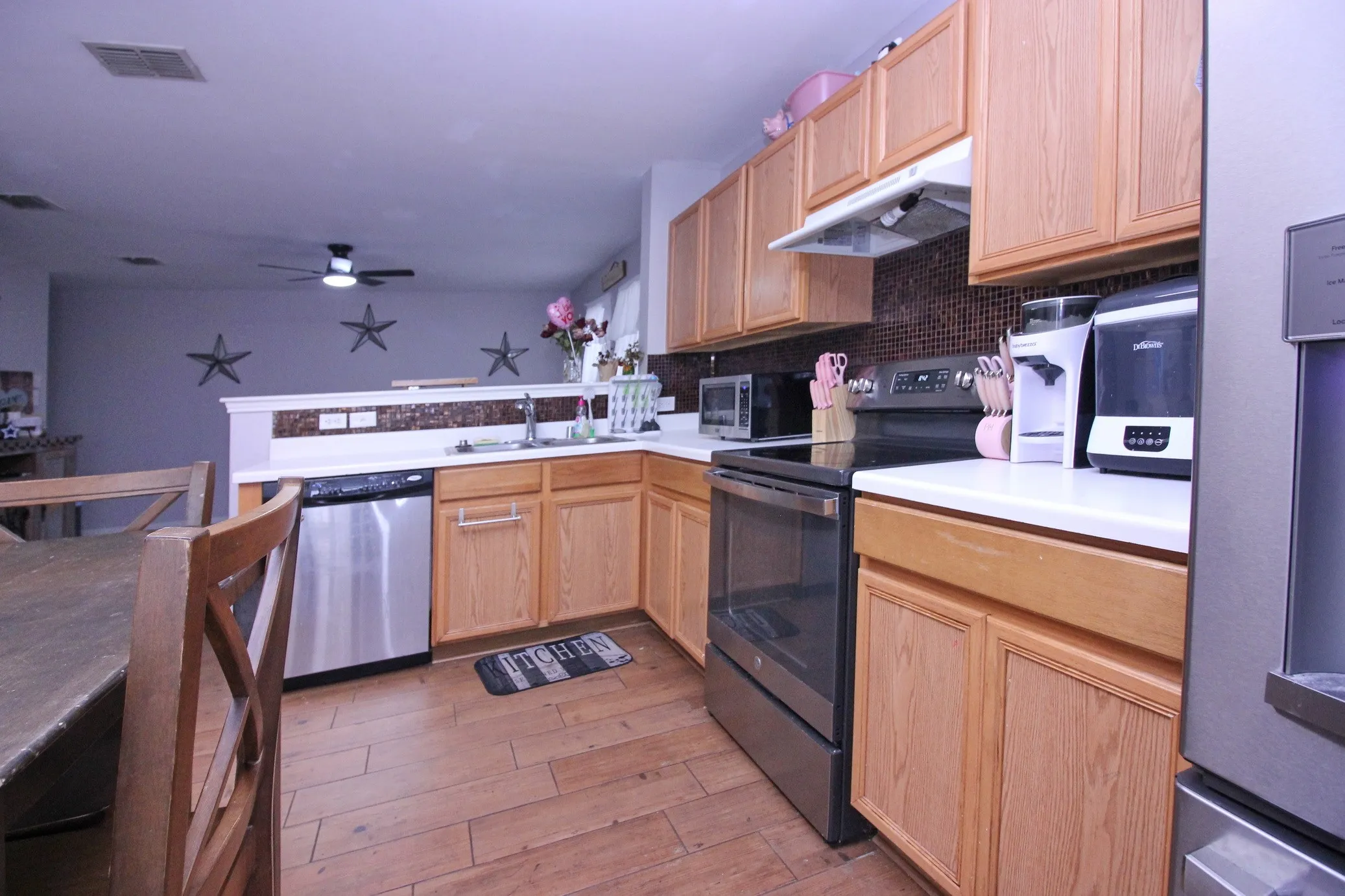 Kitchen featuring wood-finish flooring, light wood cabinetry, stainless steel appliances, and solid surface countertops