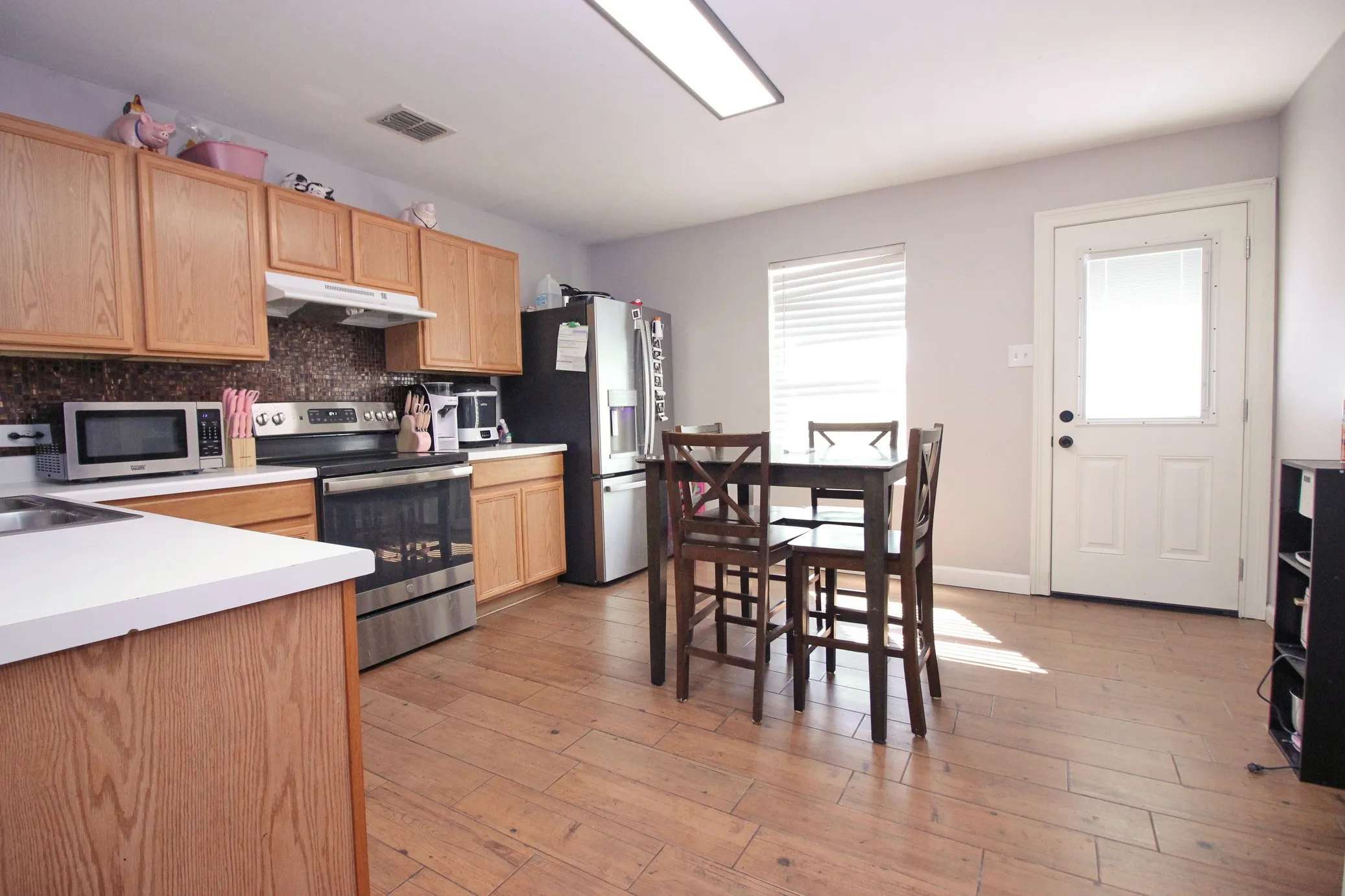 Kitchen featuring wood-finish flooring, light wood cabinetry, white countertops, and a mosaic tile backsplash
