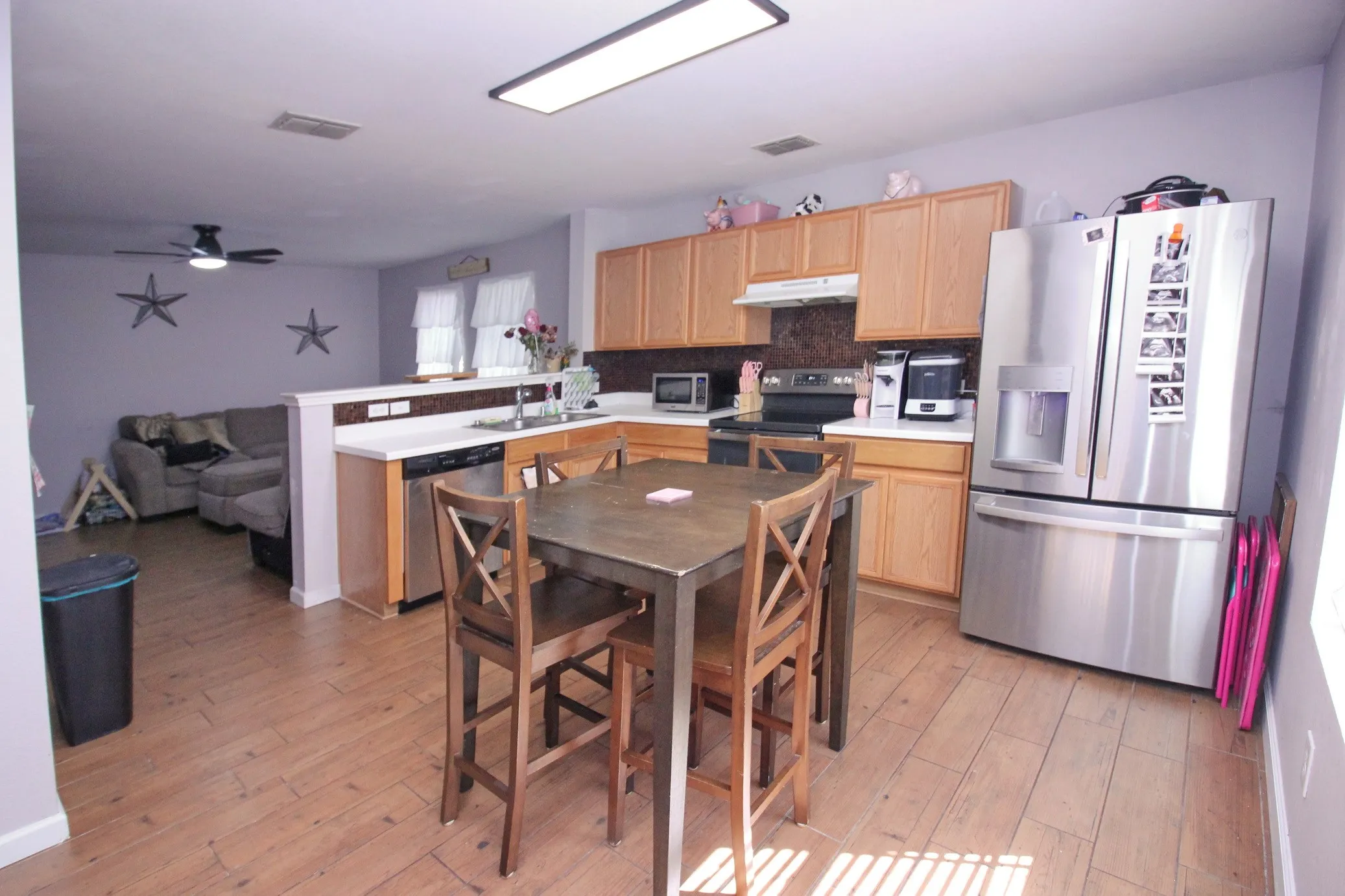 Kitchen featuring wood-finish flooring, wood cabinetry, stainless steel appliances, and a breakfast bar with white countertops