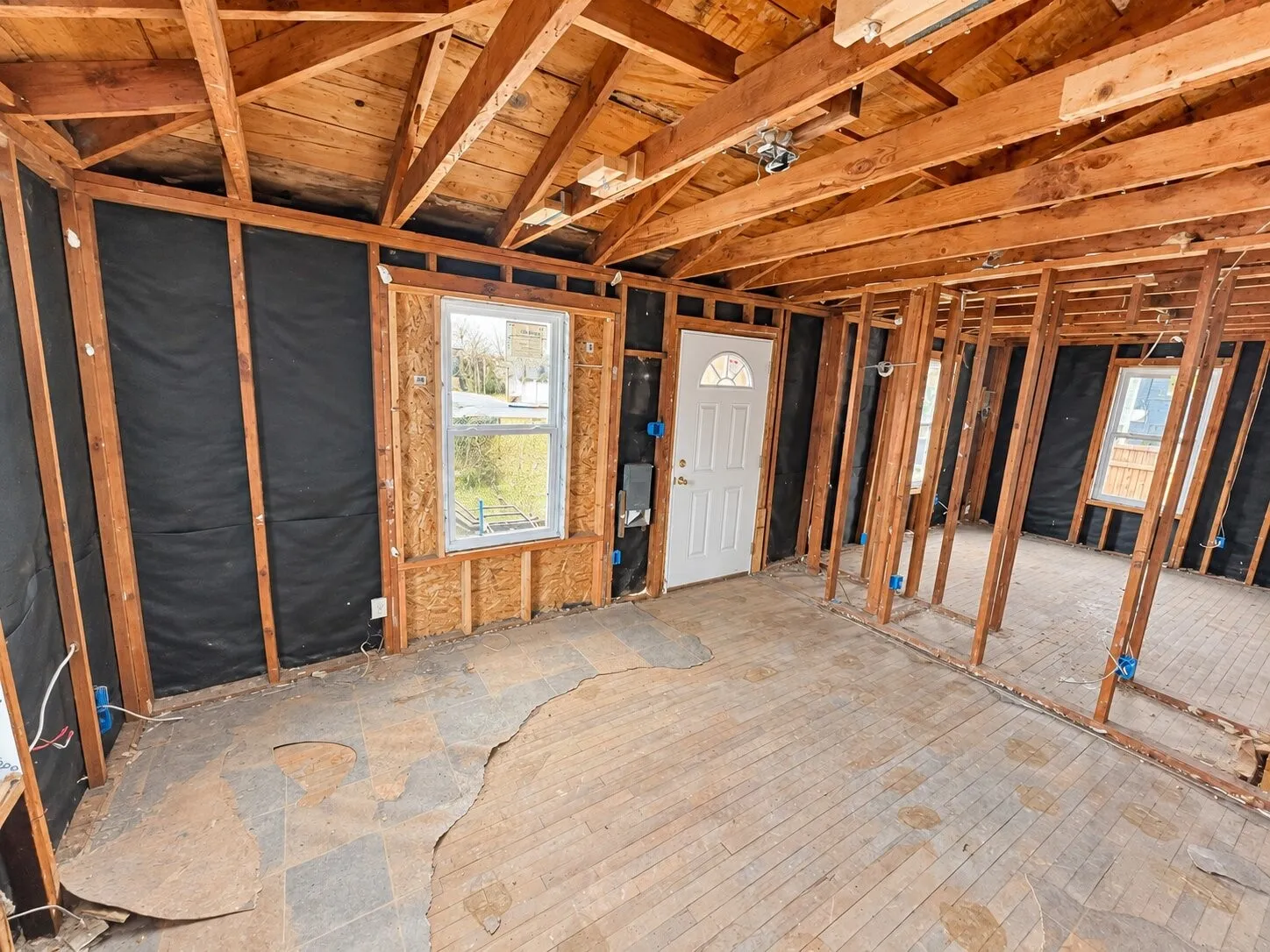 Exposed wood framing, visible ceiling joists, and a white entry door with an arched glass insert