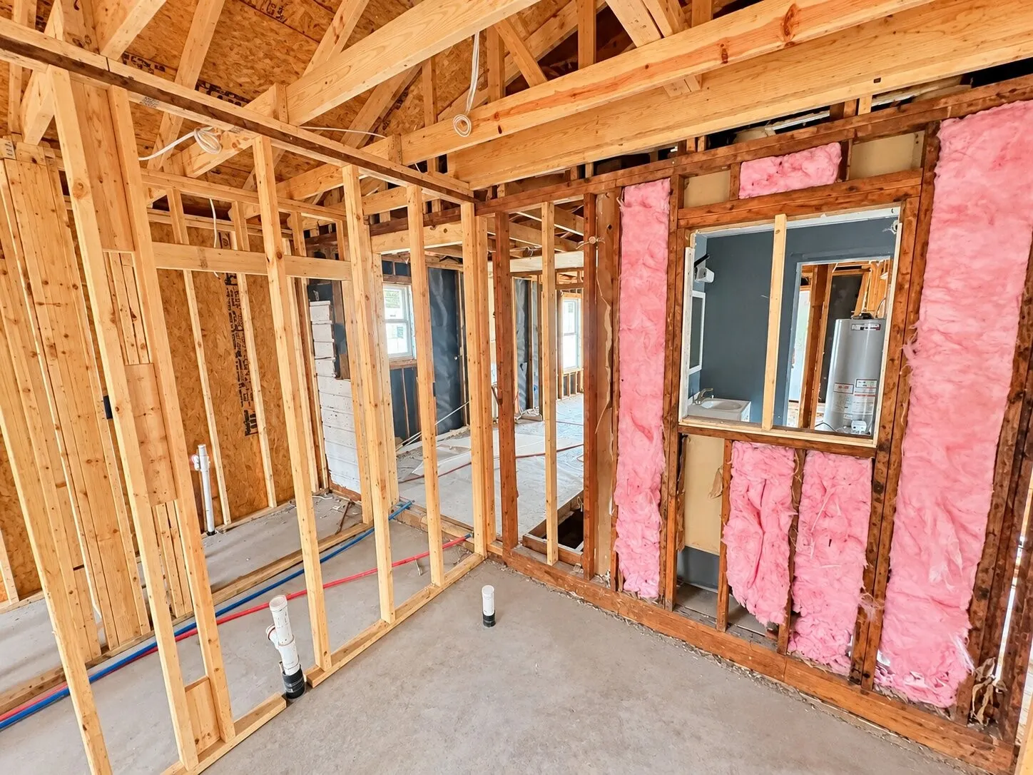 Exposed wood framing, visible plumbing lines, and attic trusses