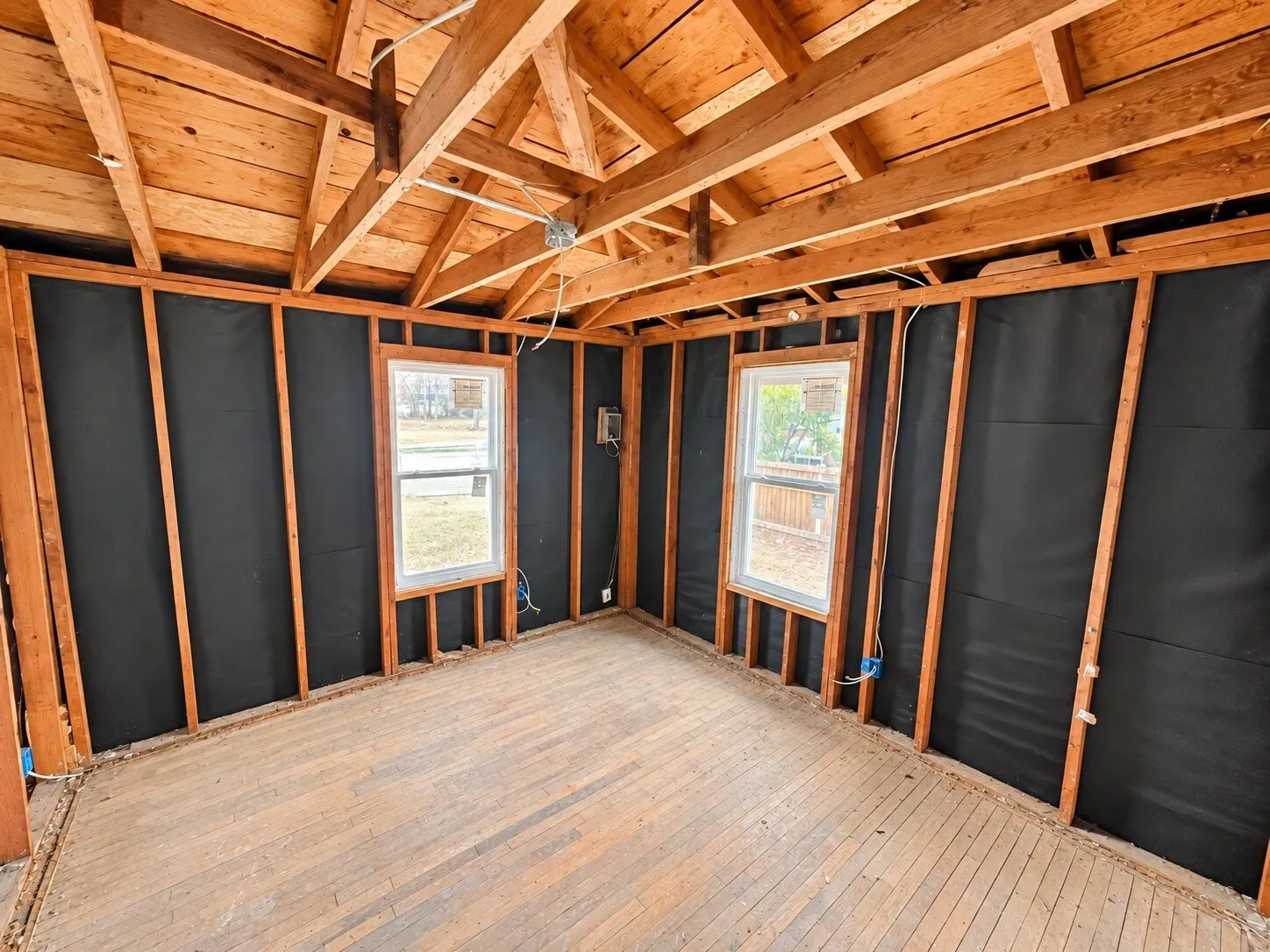 Exposed wood-frame construction with two windows, original wood flooring, and visible ceiling joists