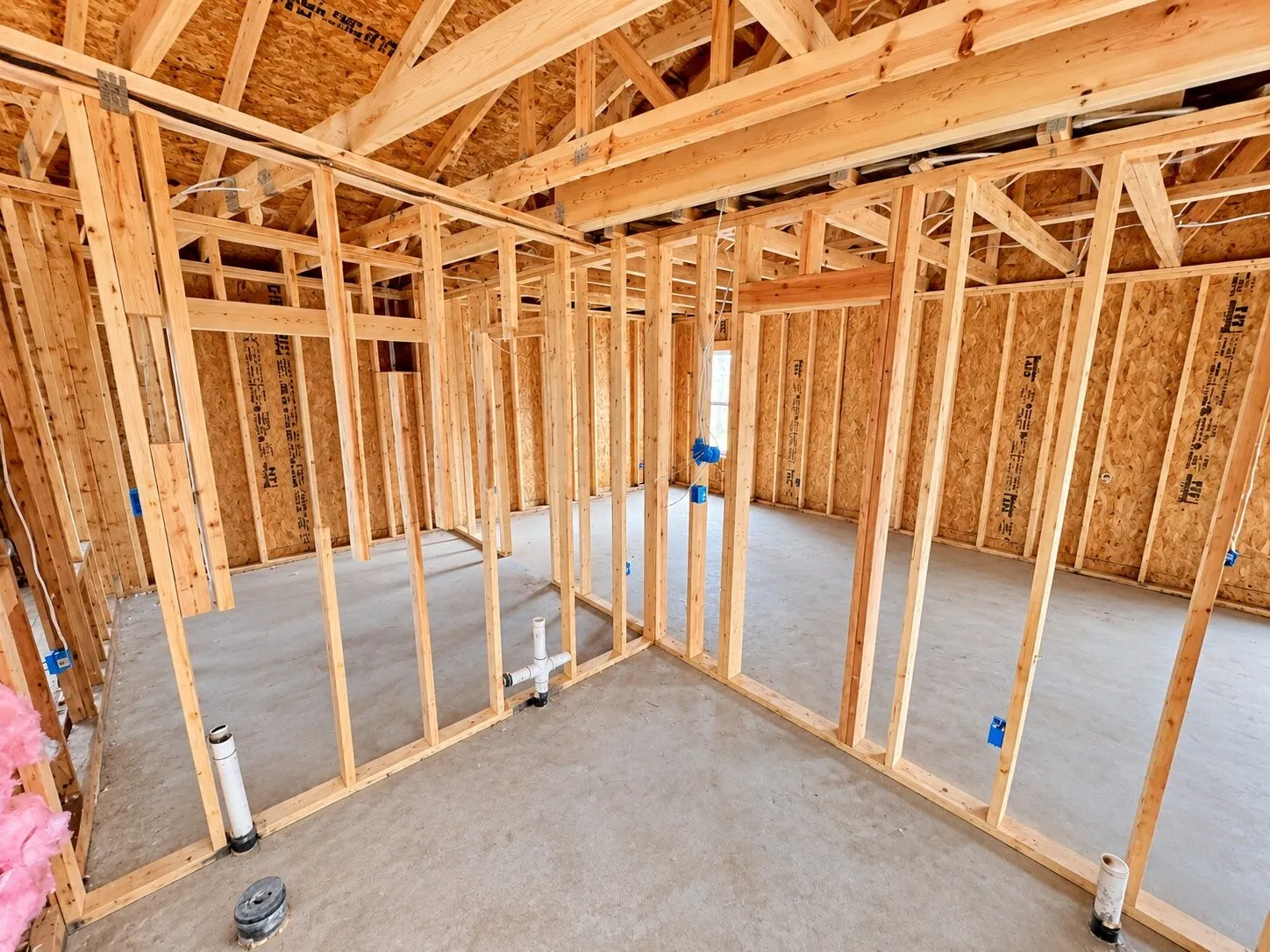 Unfinished interior framing with exposed wooden studs, concrete flooring, and visible plumbing rough-ins