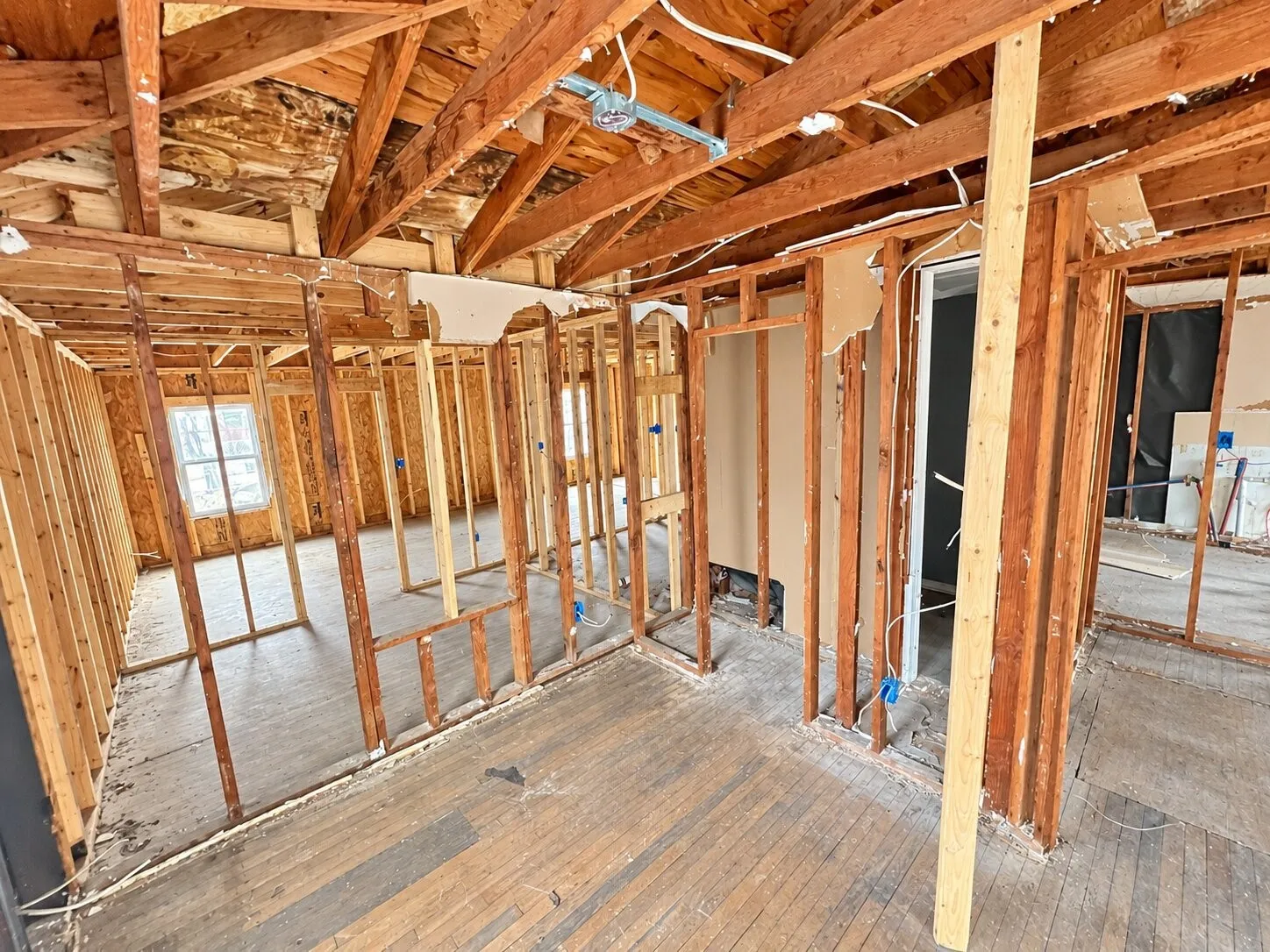 Exposed wood framing and ceiling rafters with partial subflooring and wood-finish flooring